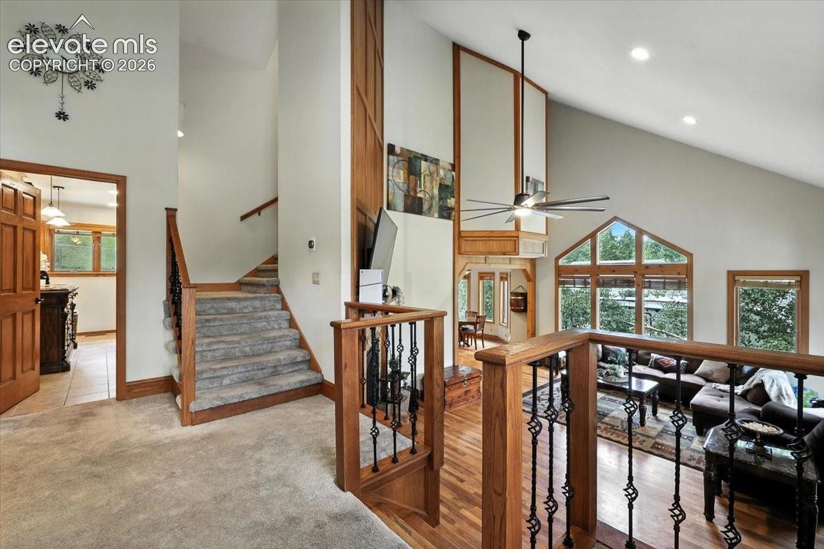 Vaulted ceilings, expansive multi-pane windows, wood-finish flooring, and a staircase featuring a wooden handrail with wrought iron balusters