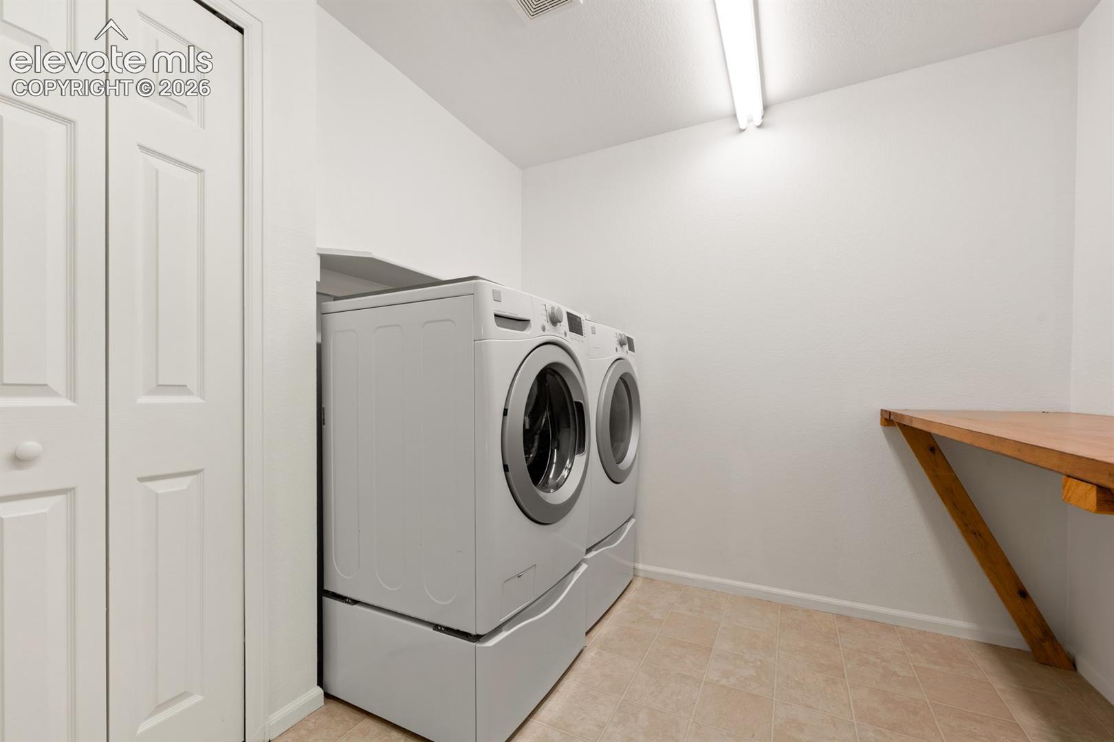 Laundry area featuring a wall-mounted wooden folding counter, bi-fold closet doors, tile flooring, and overhead utility lighting