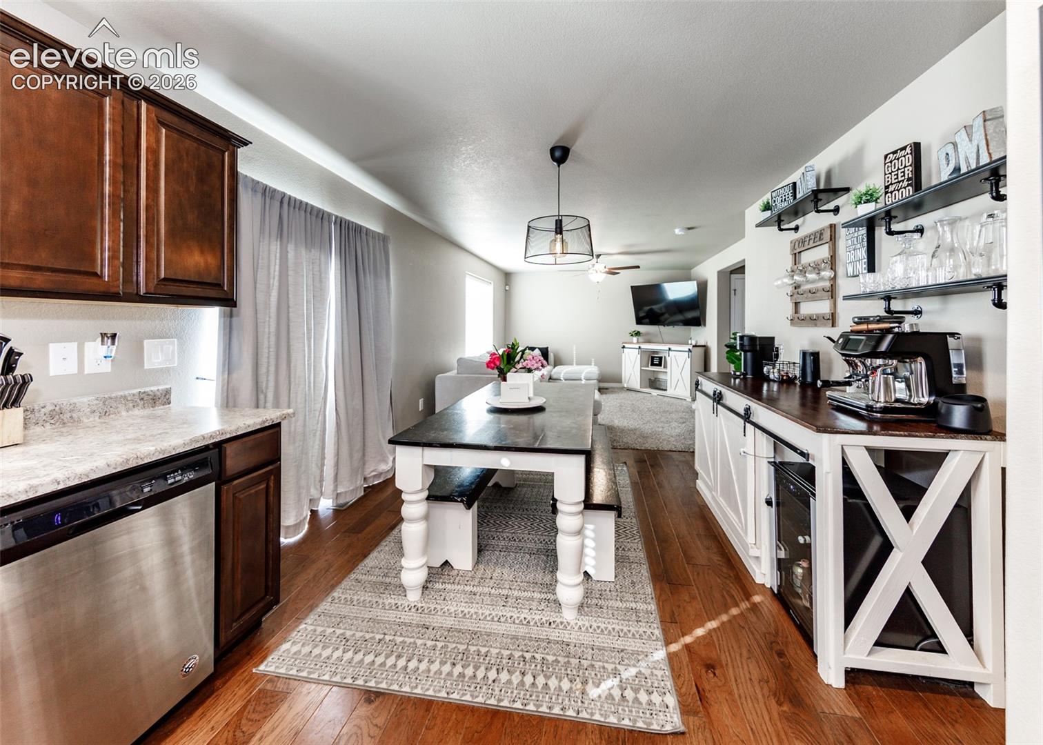 Kitchen area featuring wood-finish flooring, dark-toned cabinetry, stainless steel dishwasher, and built-in counter space with lower cabinetry and open shelving