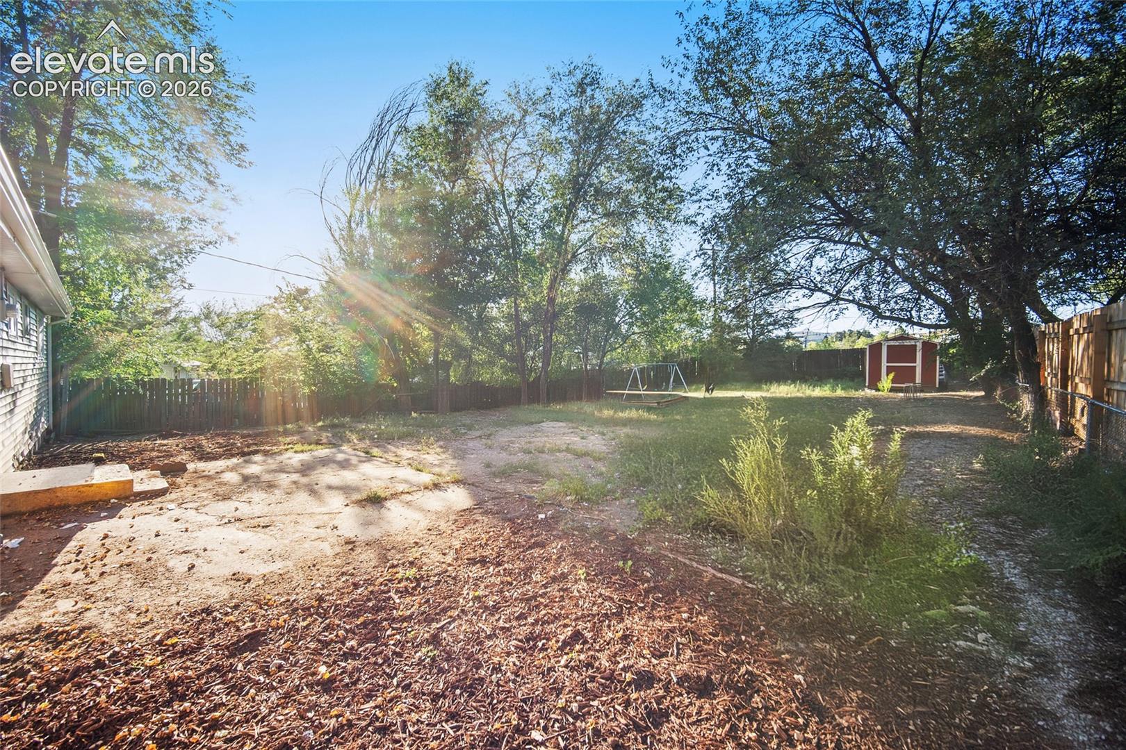 Expansive property featuring a red shed, a swing set, and a wood privacy fence