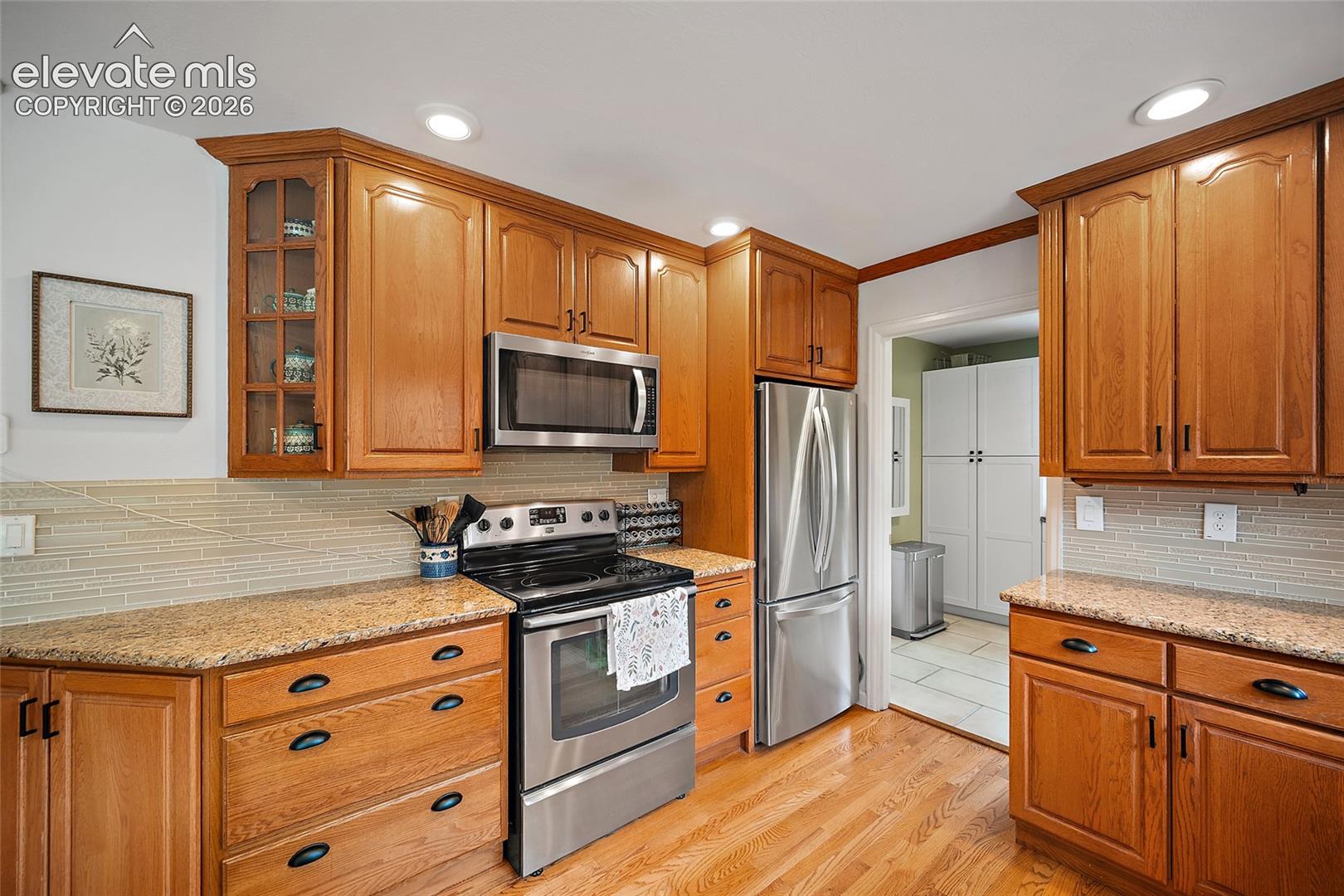 Kitchen featuring wood cabinetry, stone countertops, horizontal tile backsplash, stainless steel appliances, and wood-finish flooring