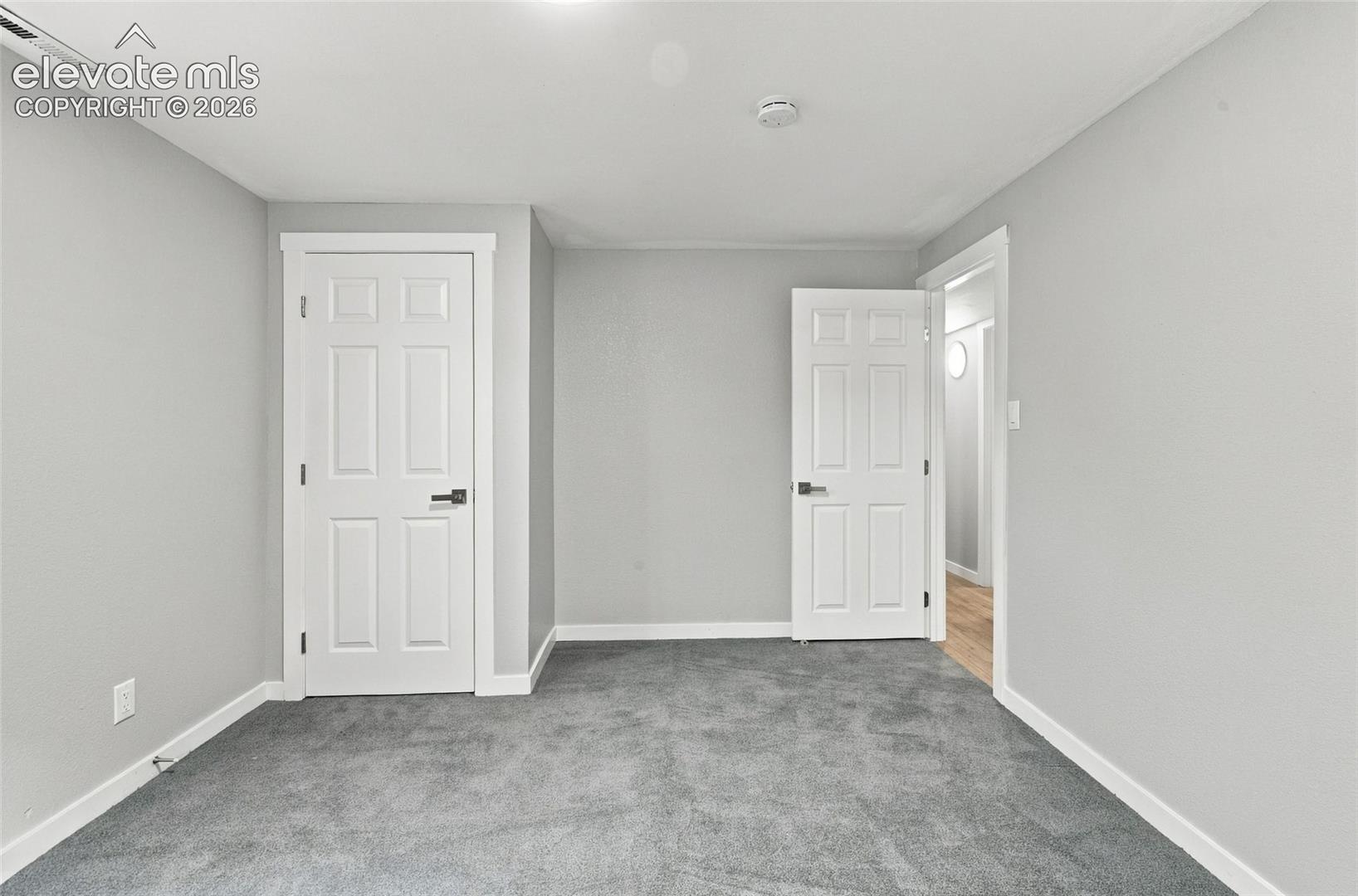 Neutral-toned walls paired with grey carpeting, featuring two six-panel interior doors with modern matte black hardware