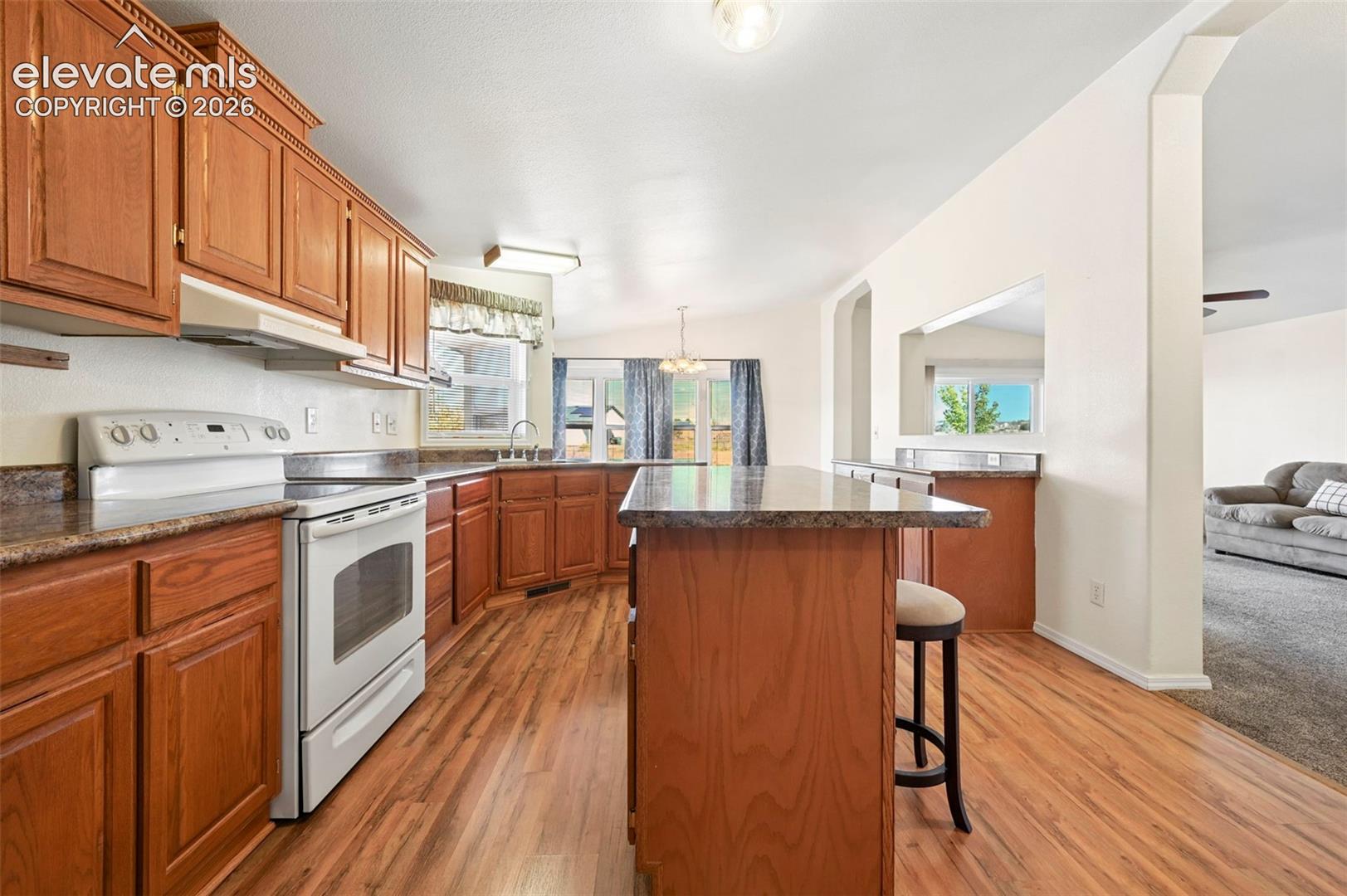 Kitchen featuring wood cabinetry, a central island with a stone-finish countertop, white appliances, and wood-finish flooring