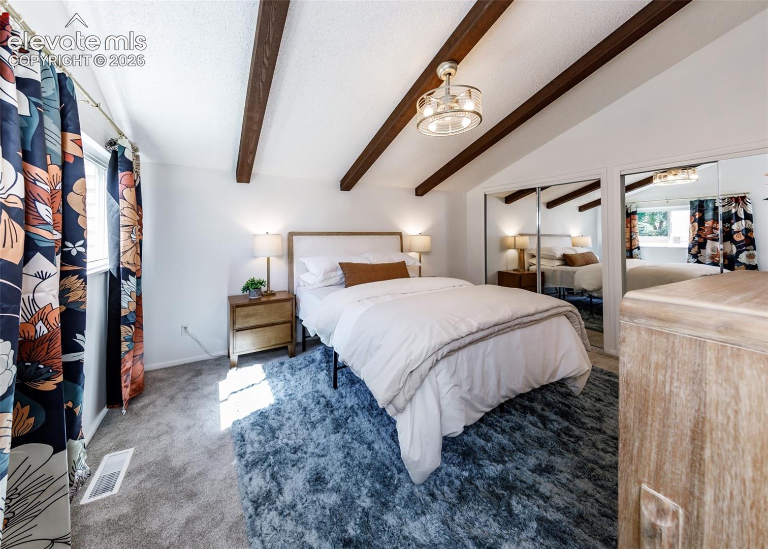 Vaulted ceilings featuring exposed wood beams, metallic multi-light ceiling fixture, and mirrored closet doors