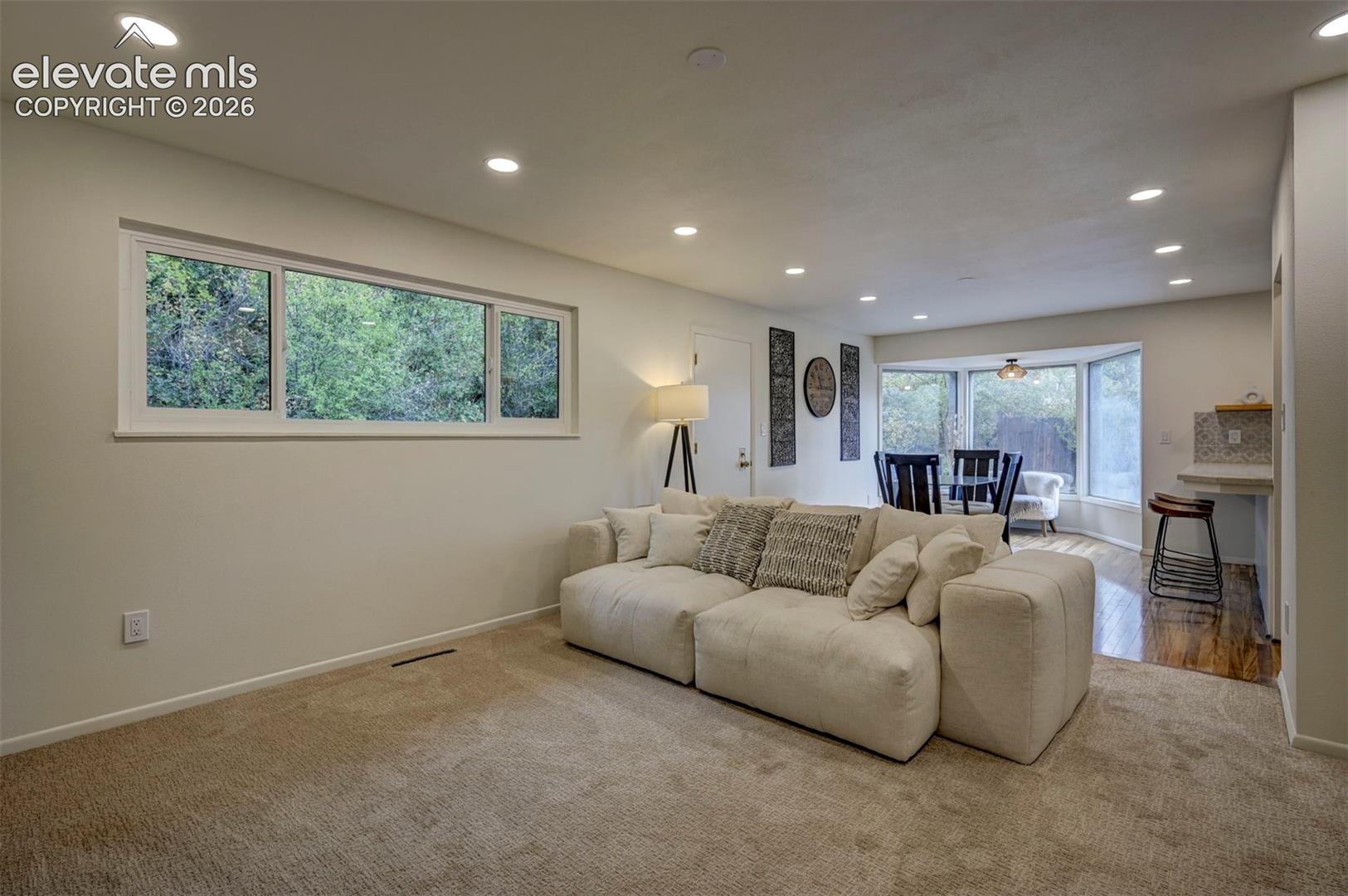 Neutral-toned interior space featuring recessed ceiling lighting, wall-to-wall carpeting, wood-finish flooring, a rectangular sliding window, and a multi-panel bay window
