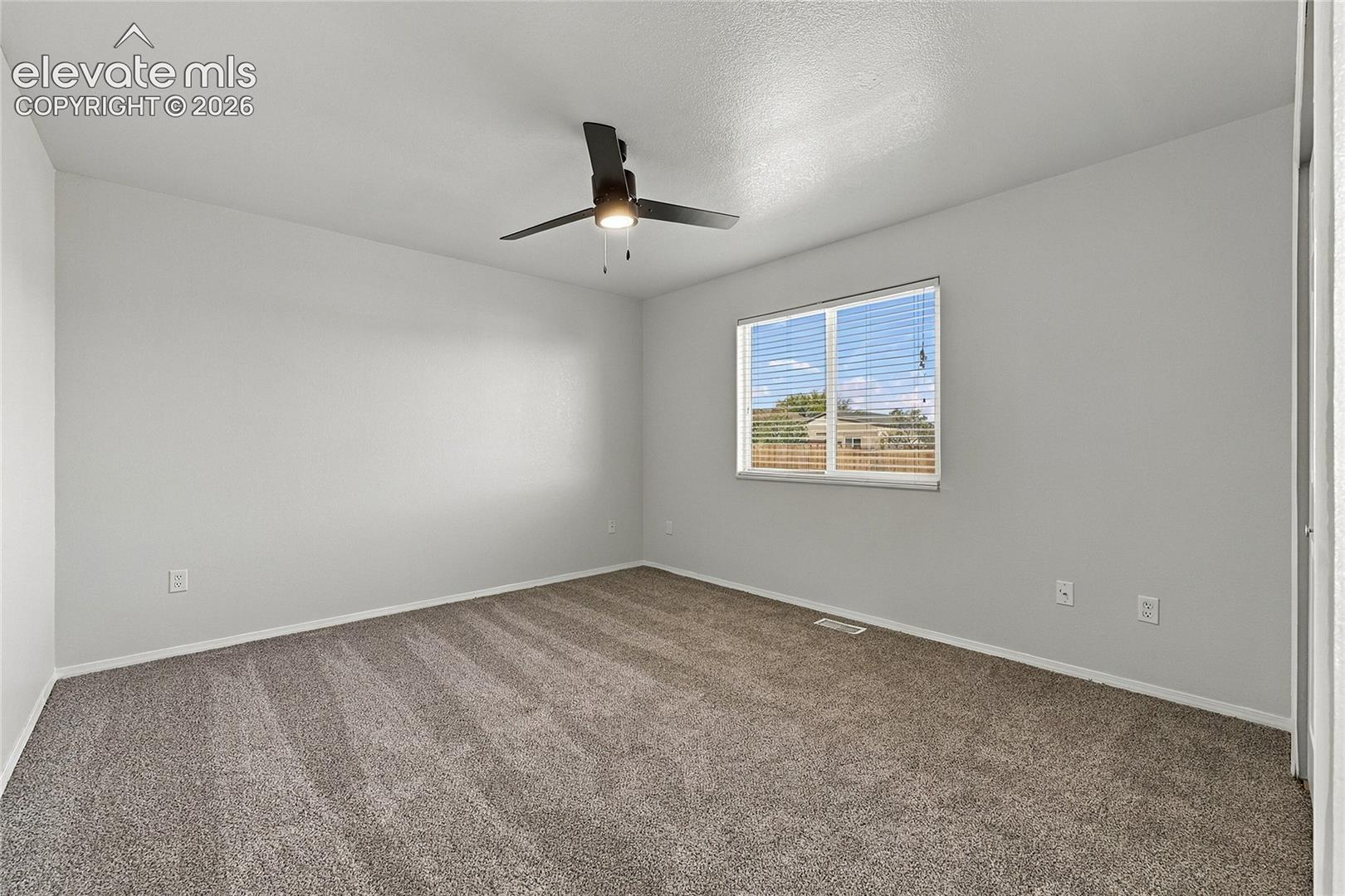 Neutral-toned interior featuring wall-to-wall carpeting, a centered ceiling fan with integrated lighting, and a window with horizontal blinds