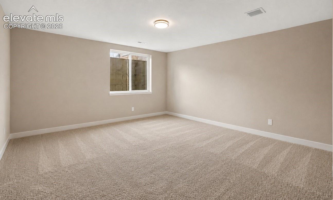 Spacious room featuring neutral-toned carpeting, light beige wall paint, a white-framed window, a ceiling-mounted light fixture, and white baseboards