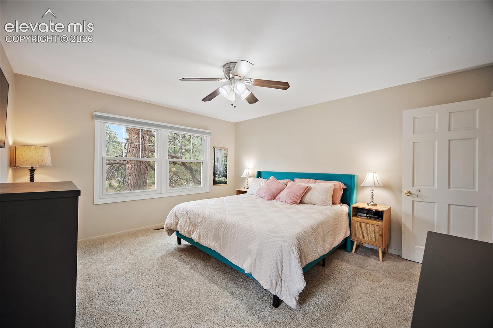 Neutral-toned interior featuring wall-to-wall carpeting, a multi-pane window with exterior scenery, a ceiling fan with integrated lighting, and a six-panel interior door