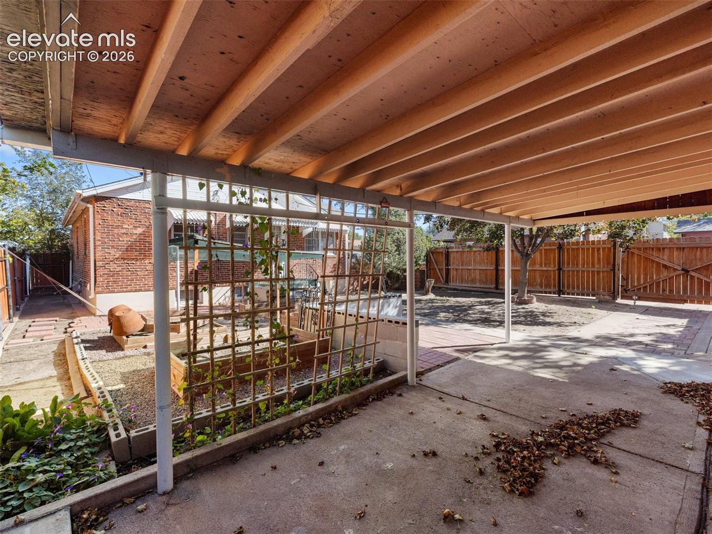 Covered patio featuring an exposed-beam wood ceiling, concrete flooring, and a decorative garden trellis, complemented by brick exterior wall and fenced yard