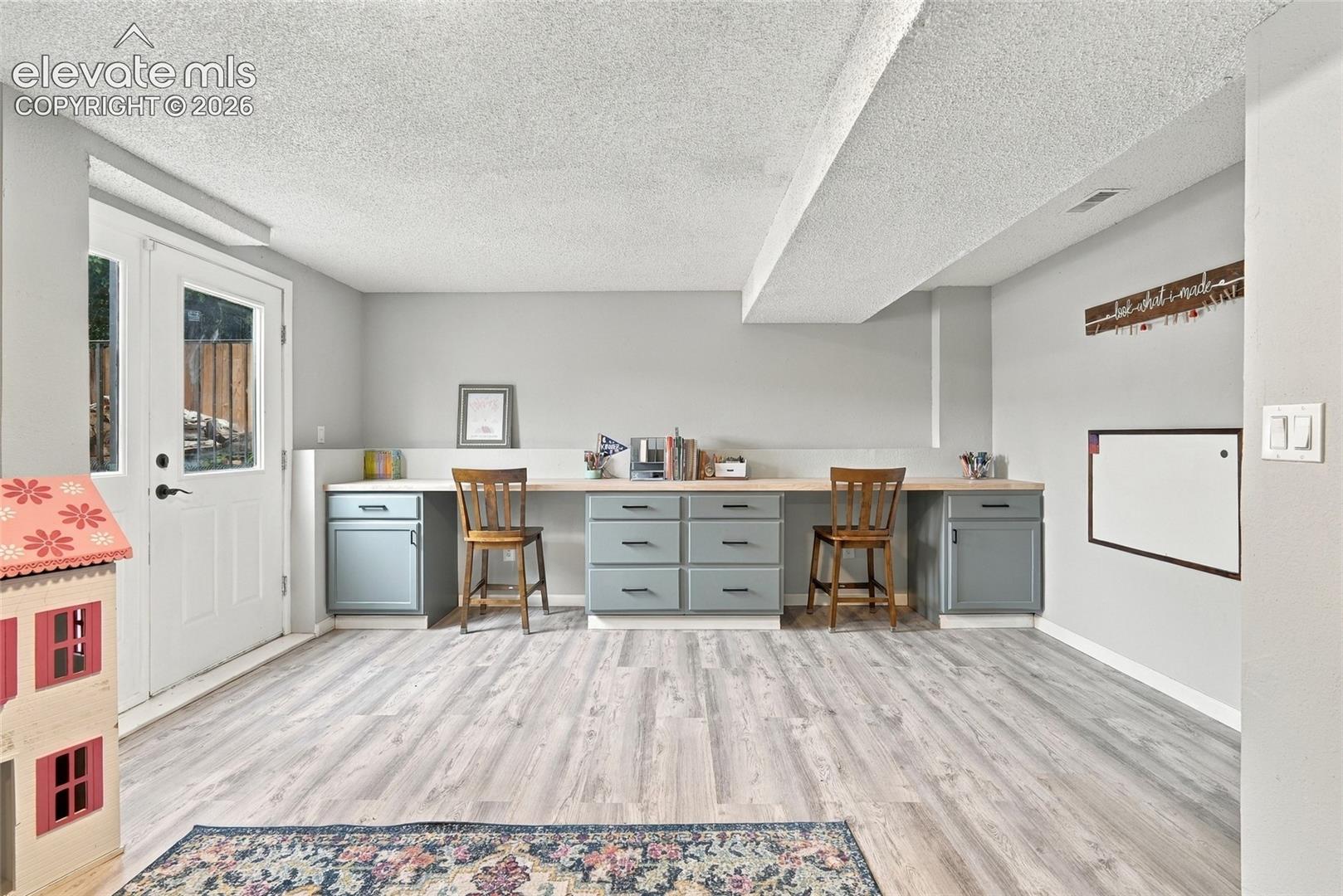 Wood-finish flooring throughout, featuring a built-in desk with lower cabinetry, and a walk-out door with clear glass panels