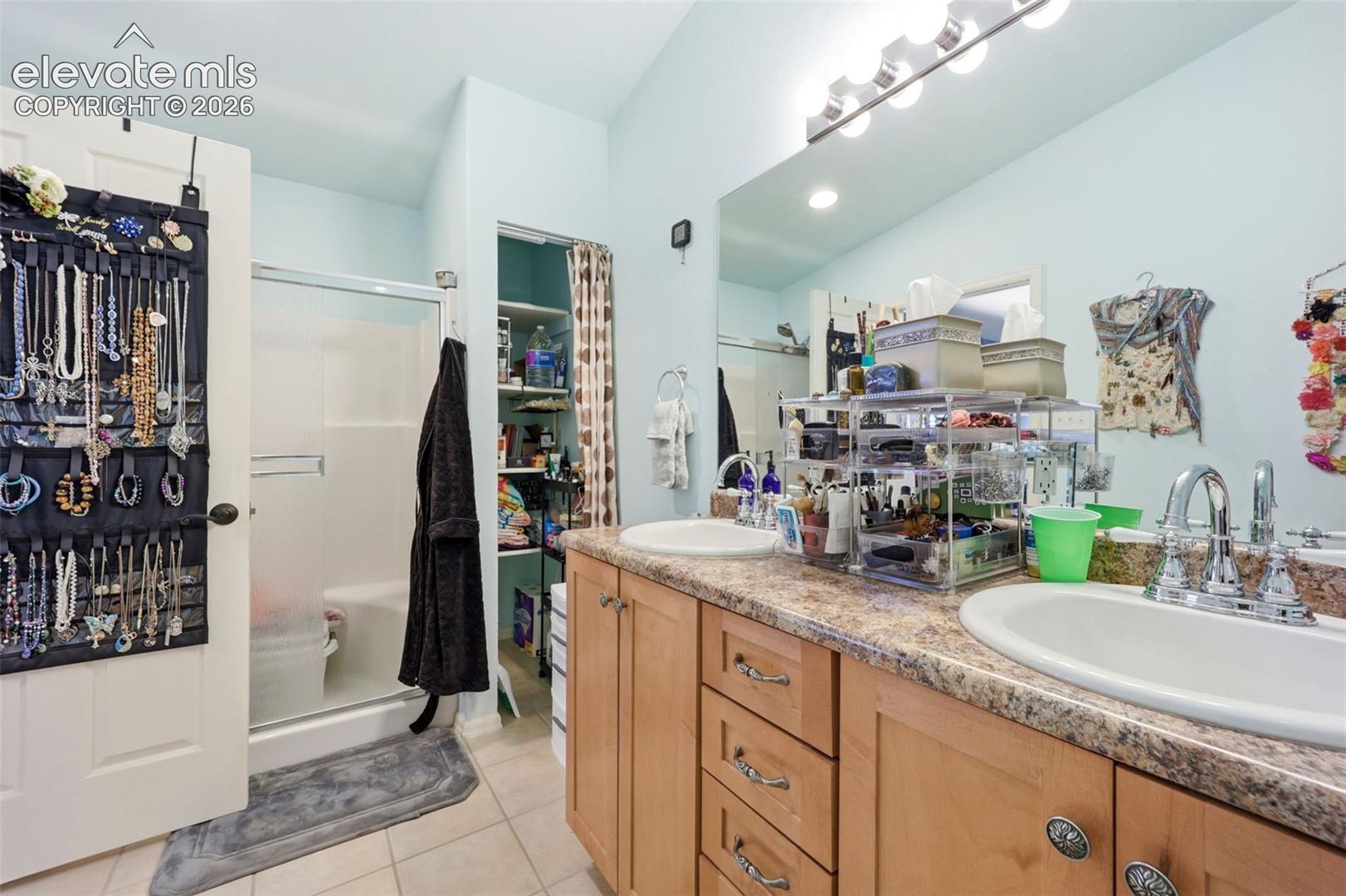 Bathroom featuring a dual vanity with light wood cabinetry, a shower with a sliding glass door, and recessed shelving