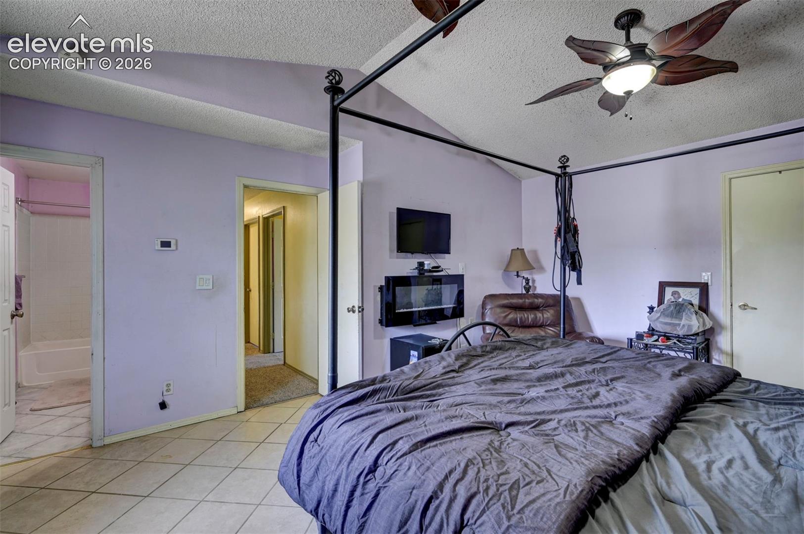 Vaulted ceiling bedroom featuring tile flooring, a wall-mounted electric fireplace, and a ceiling fan with integrated lighting