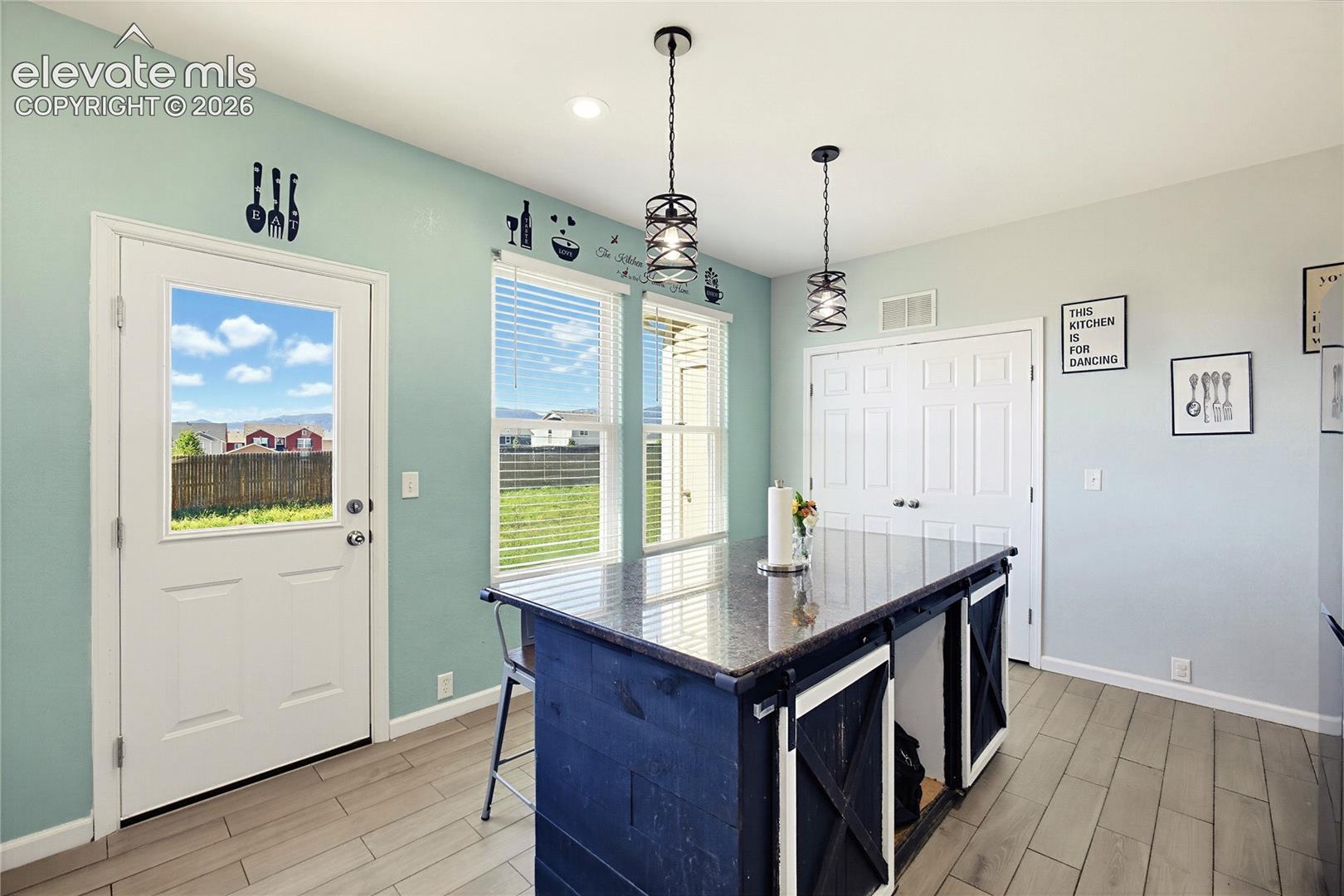 Central kitchen island with a dark countertop and barn door accents, illuminated by two pendant lights