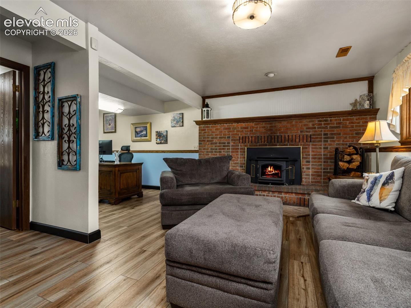 Brick fireplace with a wood-burning insert, wood-finish flooring, and exposed ceiling beams