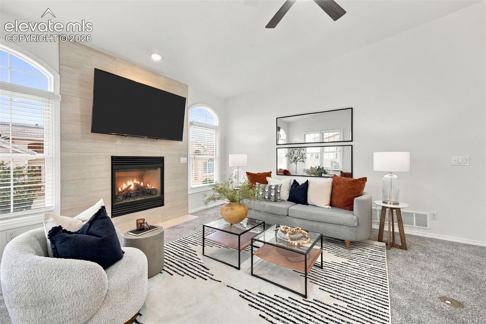 Gas fireplace with a tile surround, tall windows featuring arched transoms, and a recessed ceiling fan