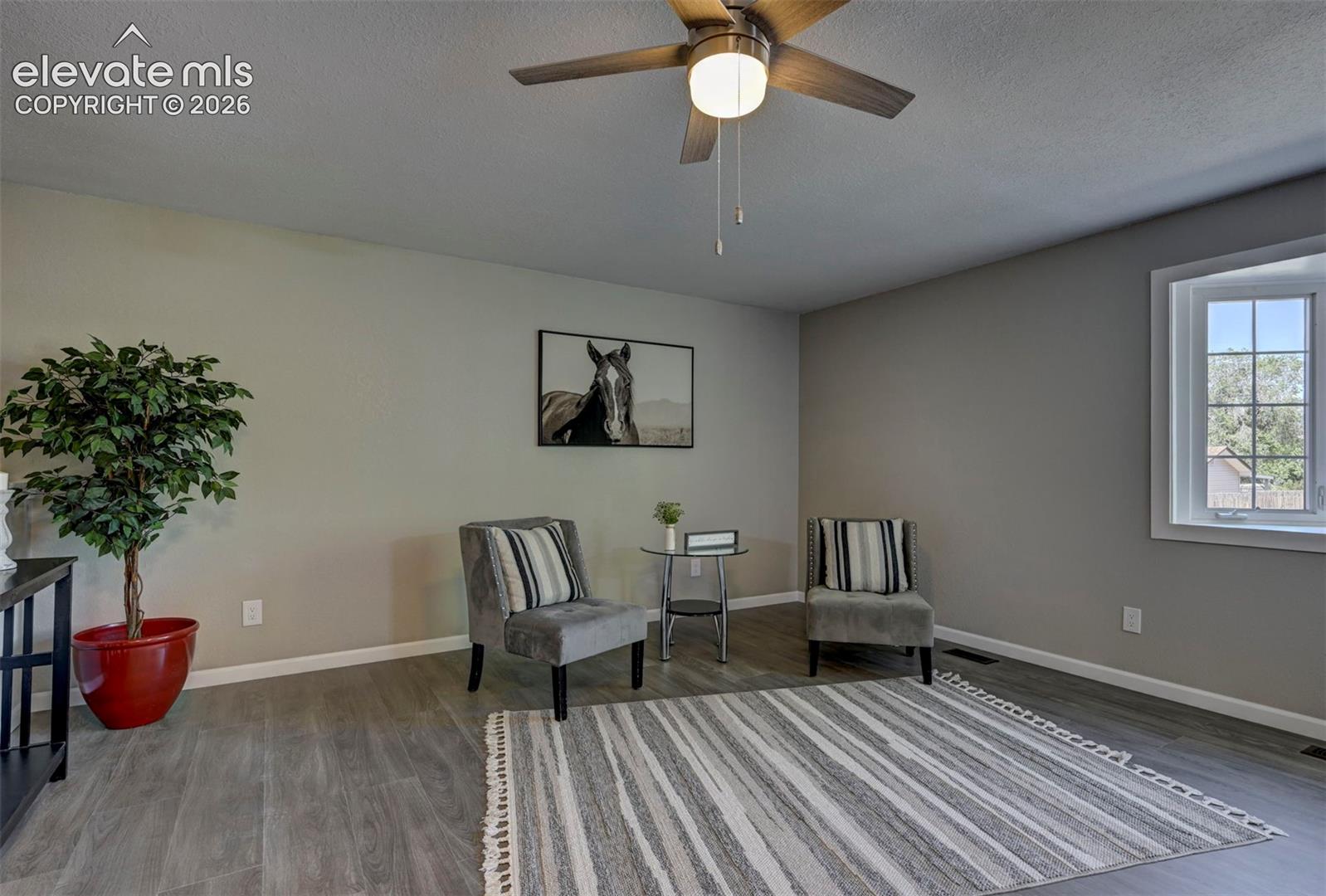 Neutral wall coloring, wood-finish flooring, multi-pane window with white trim, and a ceiling-mounted light fixture with a fan