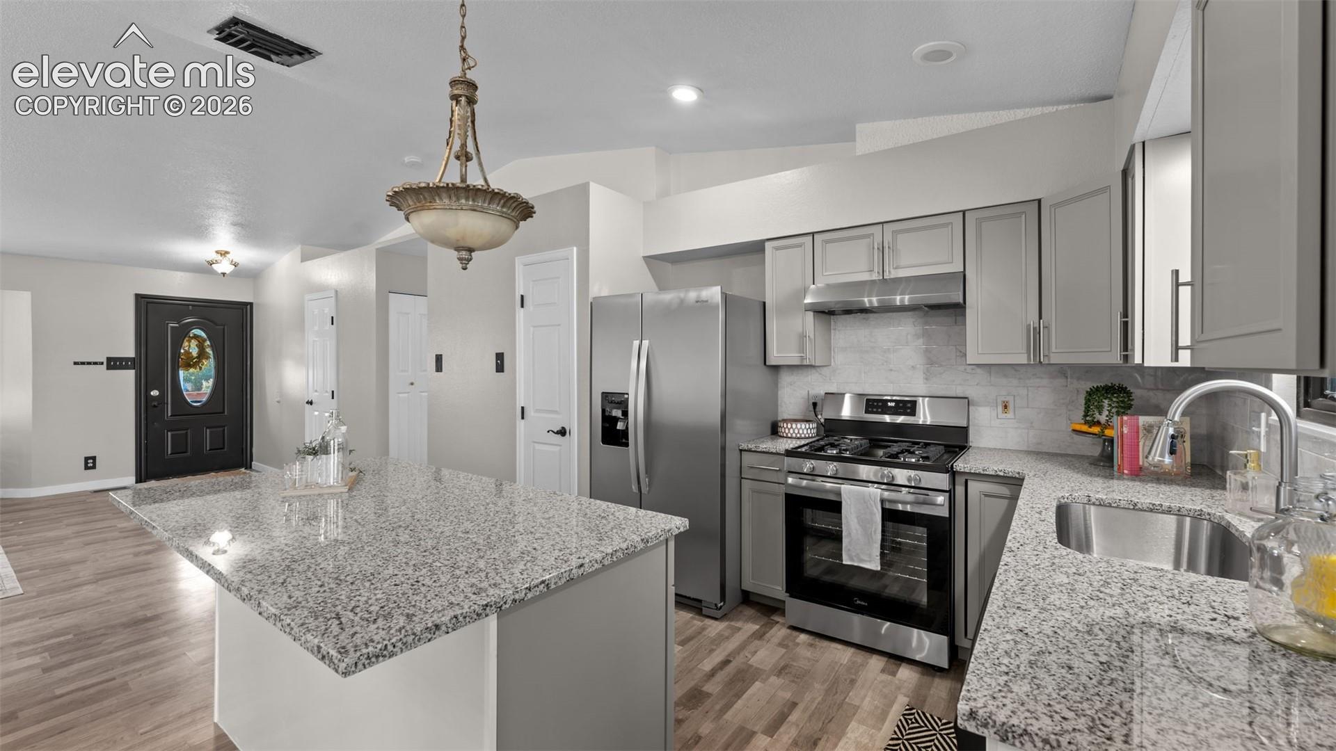 Kitchen featuring speckled stone countertops, grey cabinetry, stainless steel appliances, wood-finish flooring, and an island