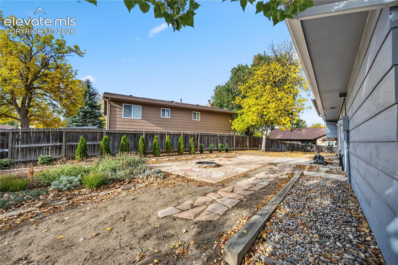 Rear exterior featuring a flagstone patio, built-in fire pit, stone-lined path, wood privacy fencing, and rock-surface ground cover