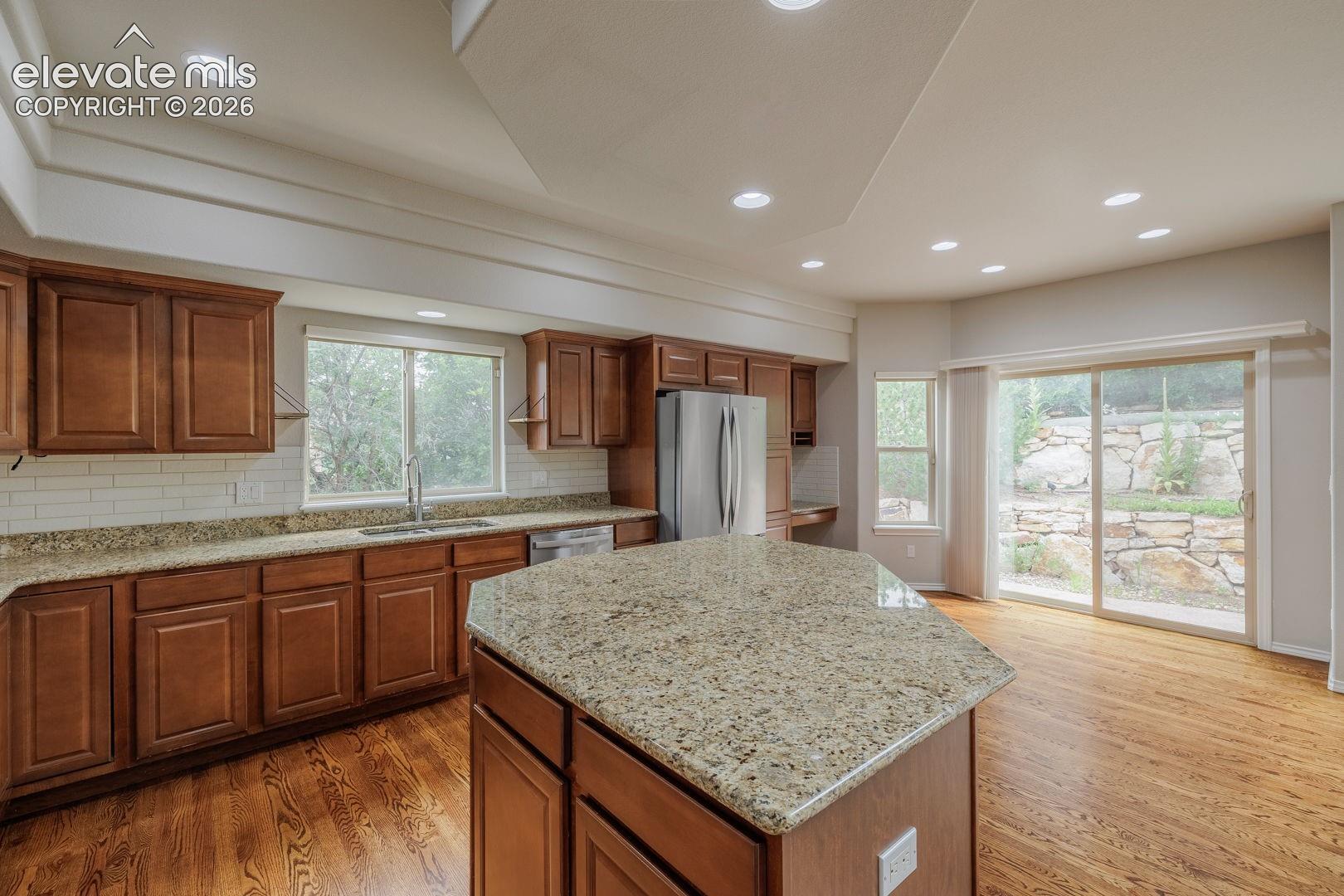 Kitchen featuring an angled island with a granite countertop, recessed lighting, wood-finish flooring, brown cabinetry, and a subway tile backsplash
