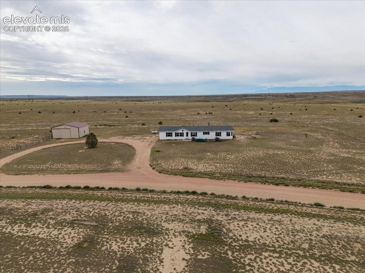Expansive rural property featuring a white residence with dark shutters, a separate metal-sided outbuilding, and a circular gravel driveway