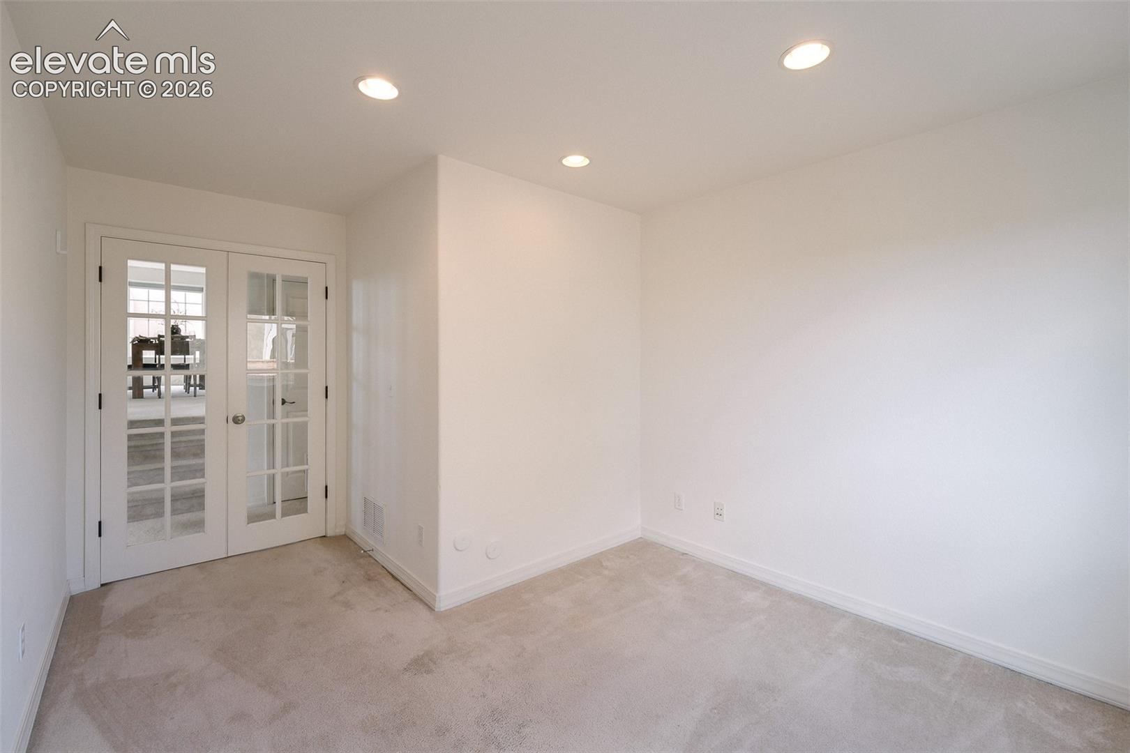 White French doors with clear glass panes, recessed ceiling lighting, light neutral-toned carpeting, and a white wall finish