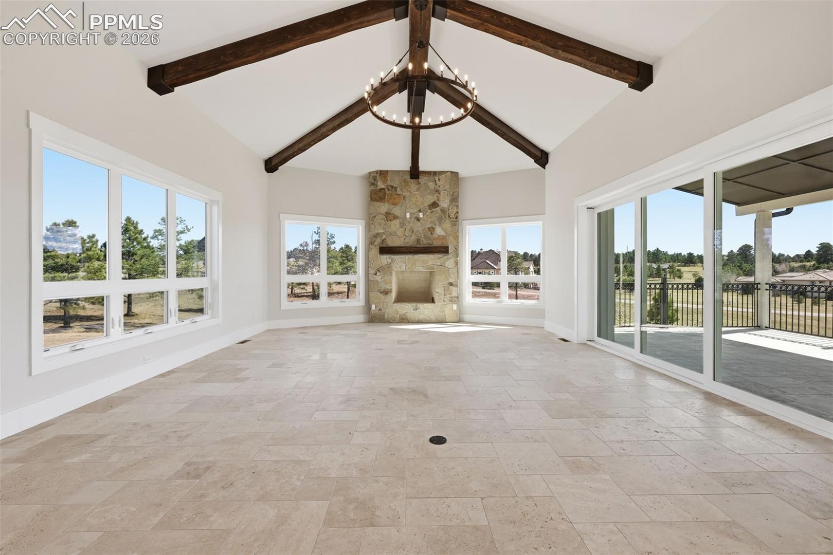 Unfurnished living room with stone tile flooring, a stone fireplace, hanging lights, and vaulted ceiling