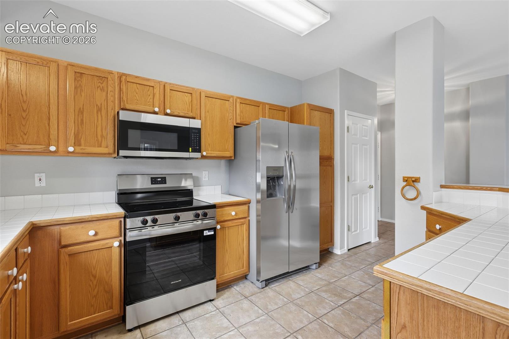 Wood-finish cabinetry, stainless steel appliances, tile flooring, and a tile countertop