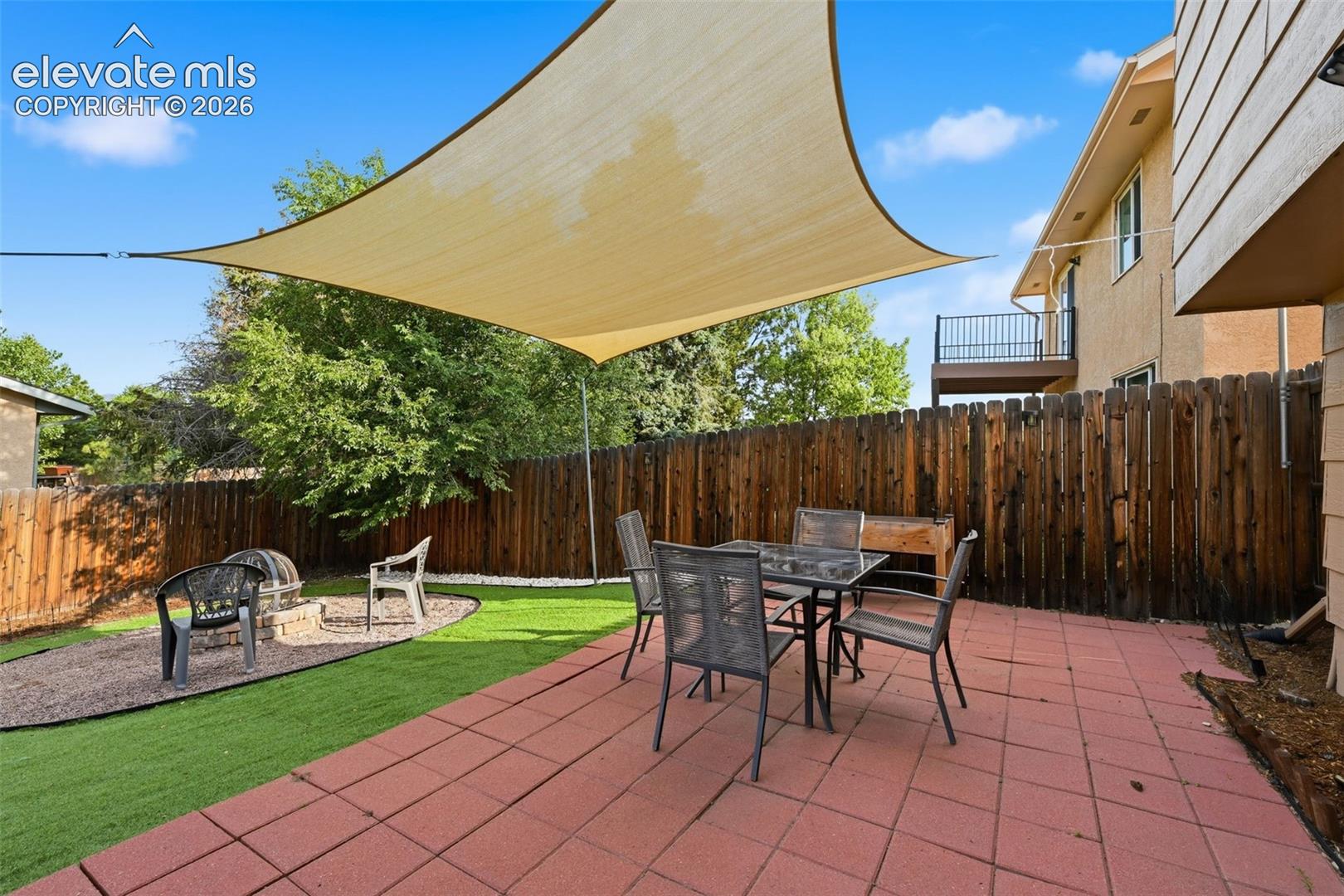 Expansive backyard featuring a large red paver patio, artificial turf, and a gravel fire pit area