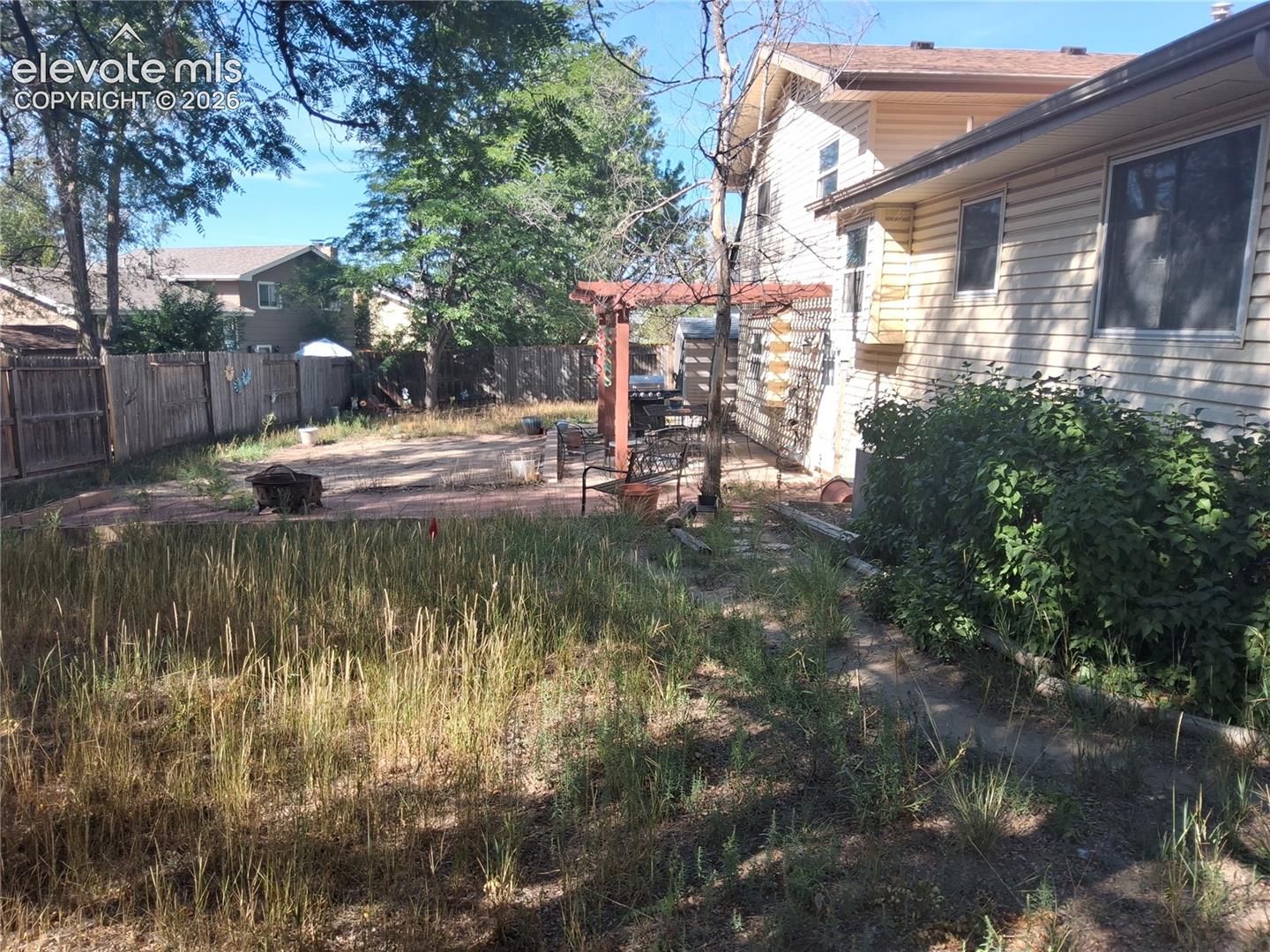 Rear exterior featuring horizontal siding, a red-toned brick patio, a wooden pergola, and a fenced-in perimeter