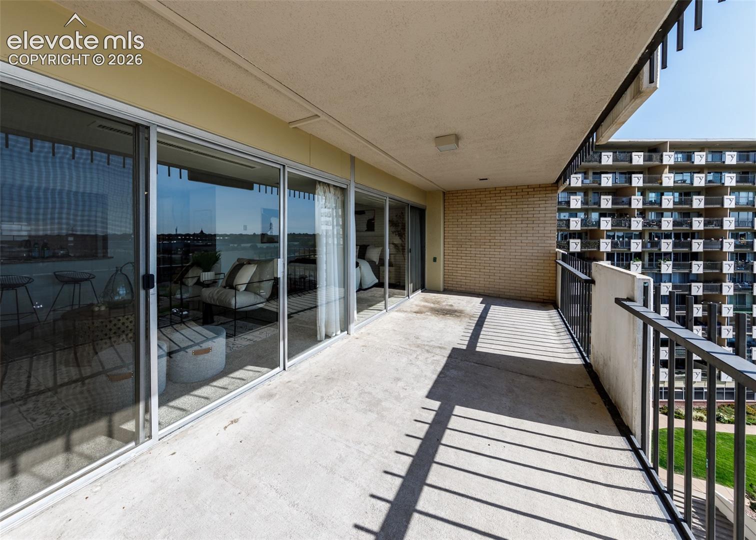 Covered balcony featuring concrete flooring, a brick side wall, and expansive sliding glass doors