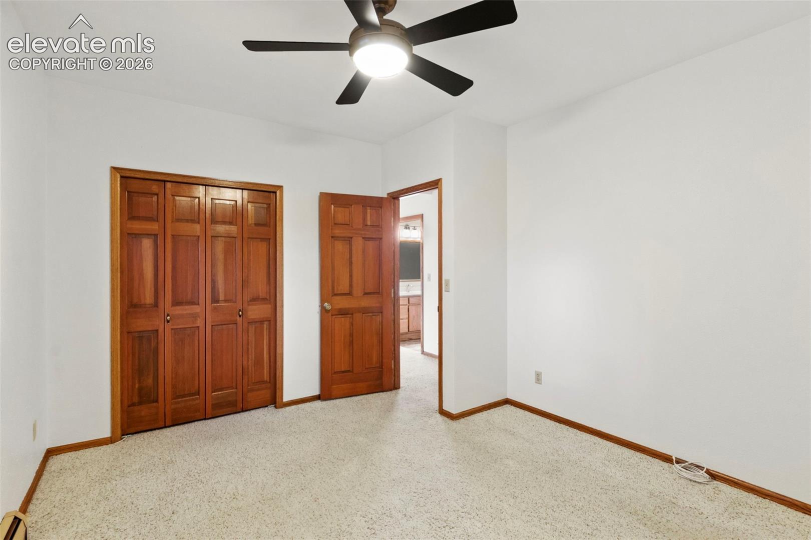 Neutral-toned carpeting, wood-finish bi-fold closet doors, six-panel wood-finish interior door, and a central ceiling fan with an integrated light fixture