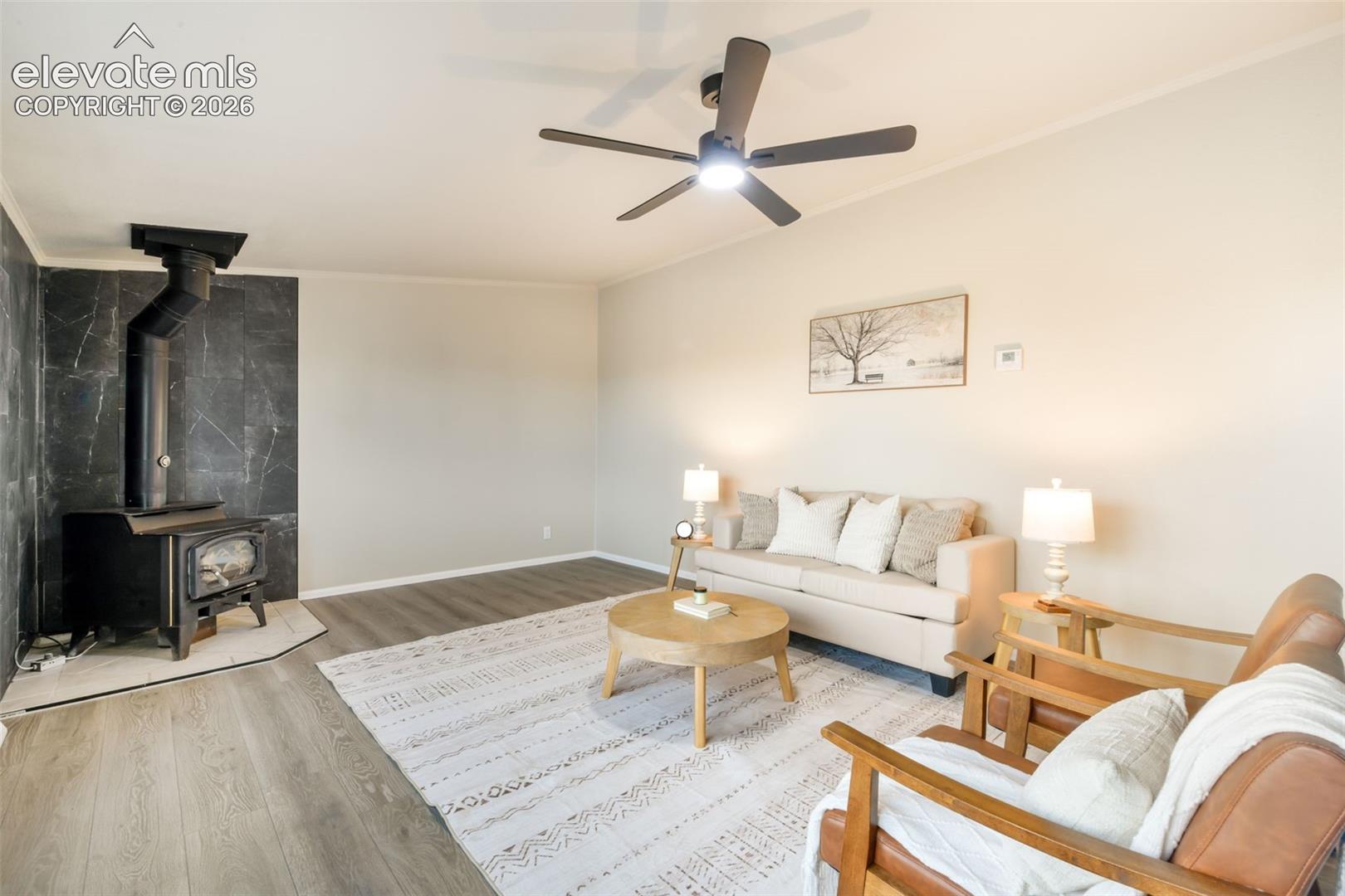 Wood-burning stove with a dark marble-look surround, wood-finish flooring, and a ceiling fan with integrated lighting
