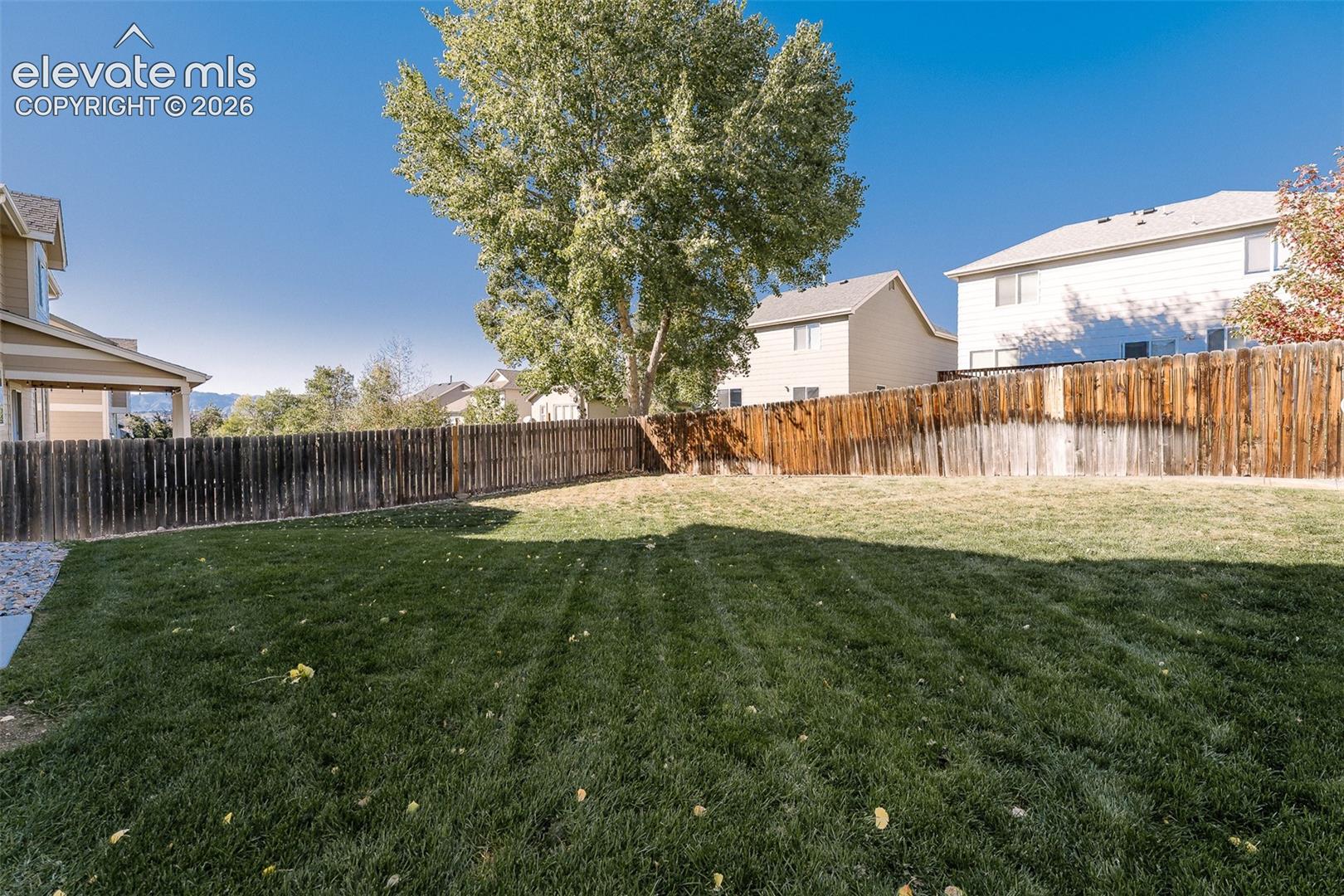 Expansive backyard featuring a manicured lawn, perimeter wood fencing, and mature trees