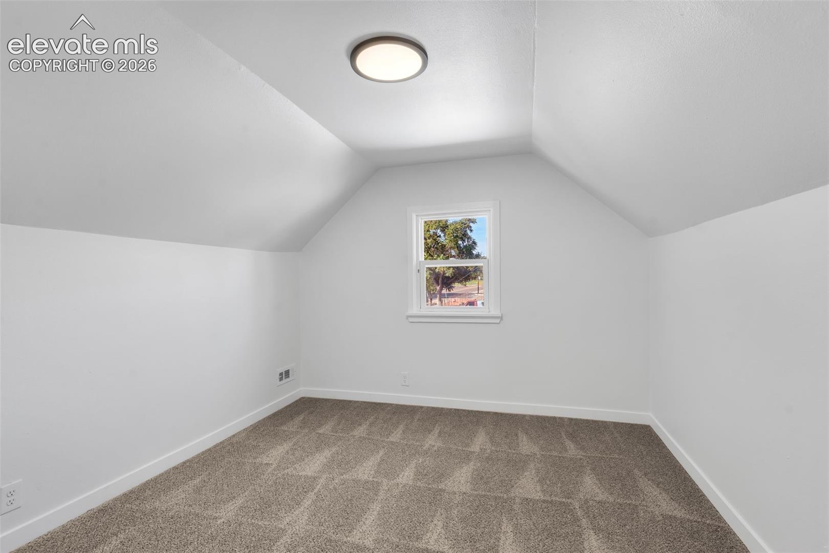 Vaulted ceiling, neutral wall tones, wall-to-wall carpeting, and a single window with exterior casing