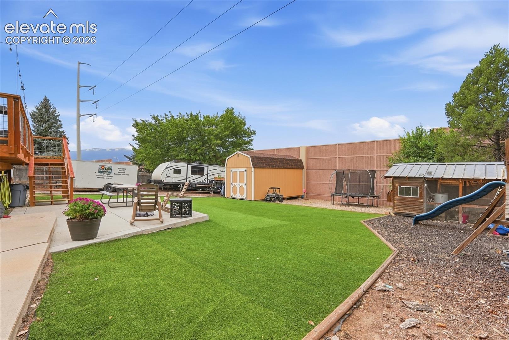 Expansive backyard featuring a manicured artificial turf lawn, concrete patio, and a tiered wooden deck
