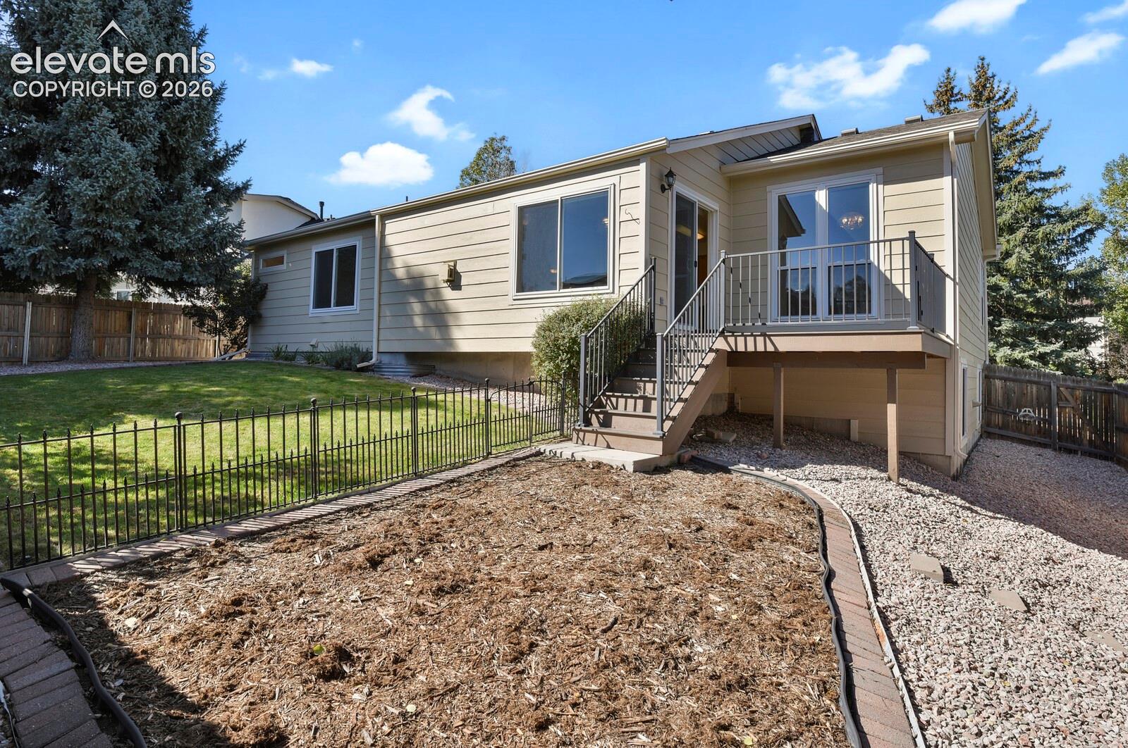 Exterior siding with multiple windows, elevated deck with railing, exterior staircase, and a fenced lawn area