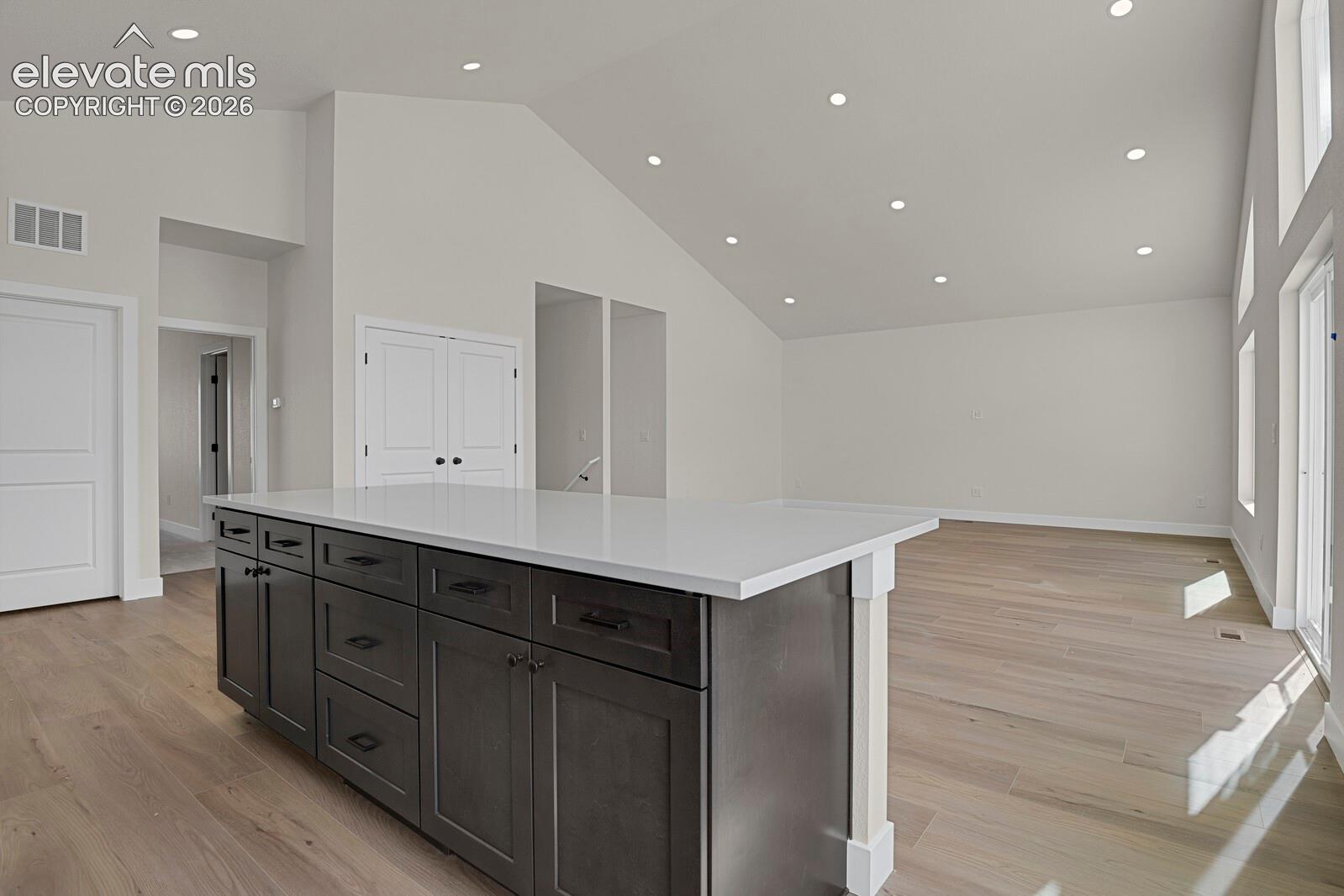 Vaulted ceilings featuring recessed lighting, a kitchen island with stone-finish countertops, dark-tone cabinetry, and wood-finish flooring