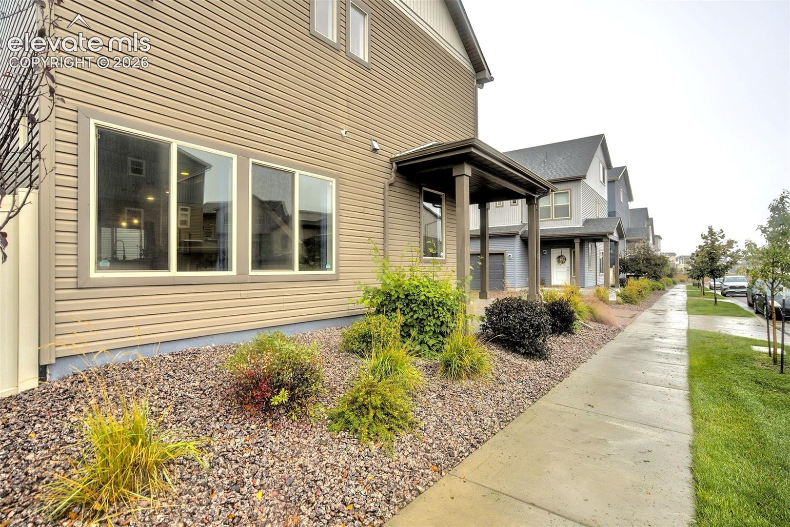 Exterior featuring horizontal siding, a covered porch with support pillars, multi-pane windows, and stone-accented landscaping