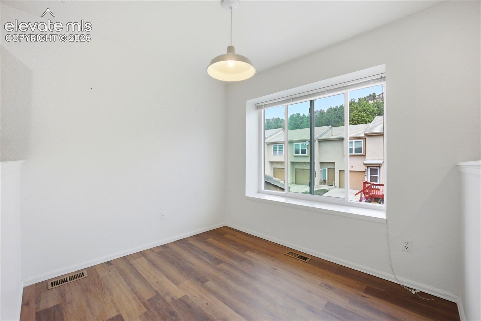 Interior space featuring wood-finish flooring, a large window with white trim, and a dome-style pendant light fixture