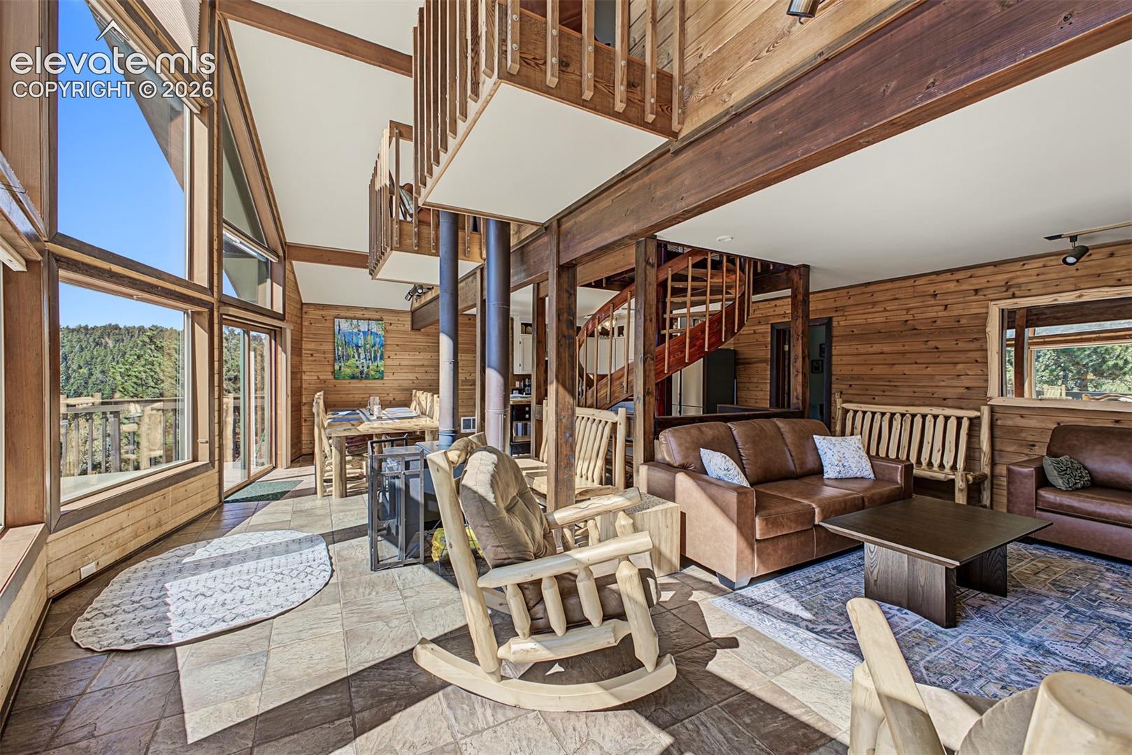 Vaulted ceilings with exposed wood beams, extensive natural wood paneling, a spiral staircase, and large picture windows