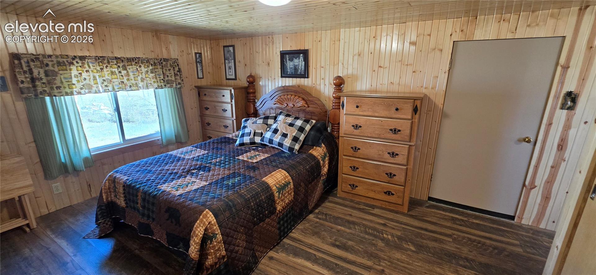 Wood-finish flooring, paneled wood walls, and a single window with a valance