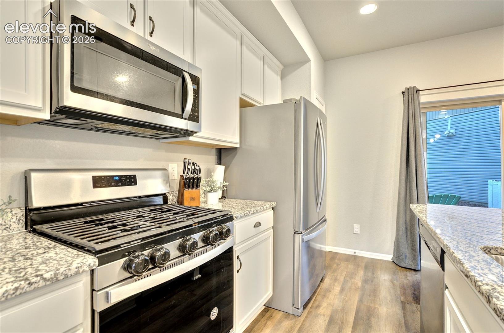 Kitchen featuring white cabinetry, stone-patterned countertops, stainless steel appliances, a gas range, and wood-finish flooring