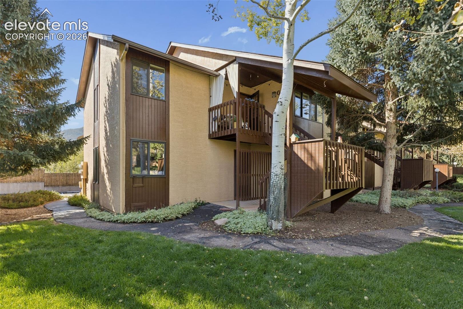 Two-story exterior with stucco and vertical wood siding, multiple private balconies, and surrounding mature trees and landscaping