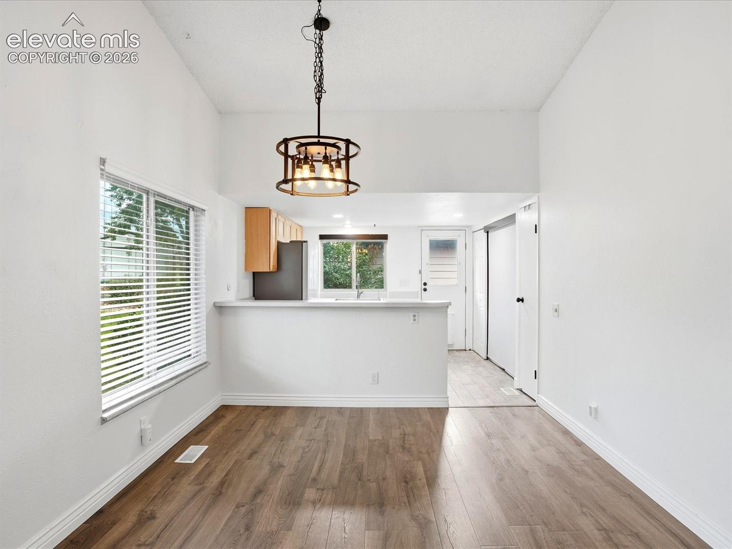 Vaulted ceilings, wood-finish flooring, industrial-style drum pendant light, white cabinetry, and a pass-through breakfast bar