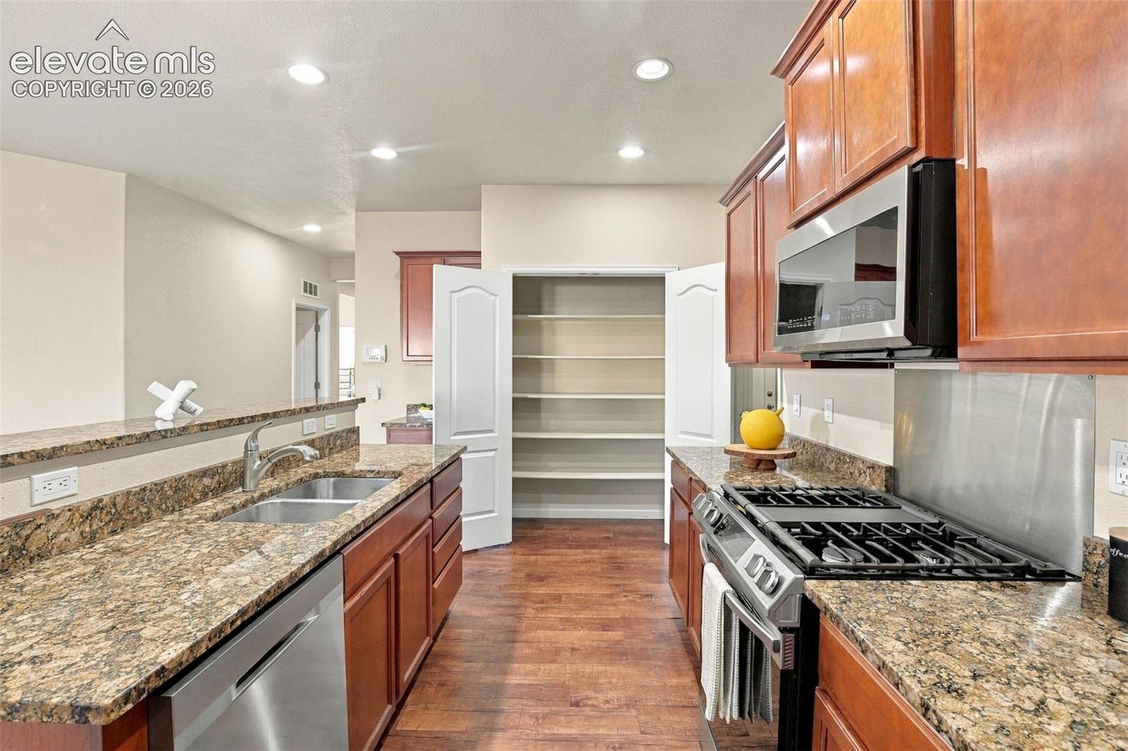 Kitchen featuring stained wood cabinetry, stone-surface countertops, built-in stainless steel appliances, and a walk-in pantry with multi-level shelving