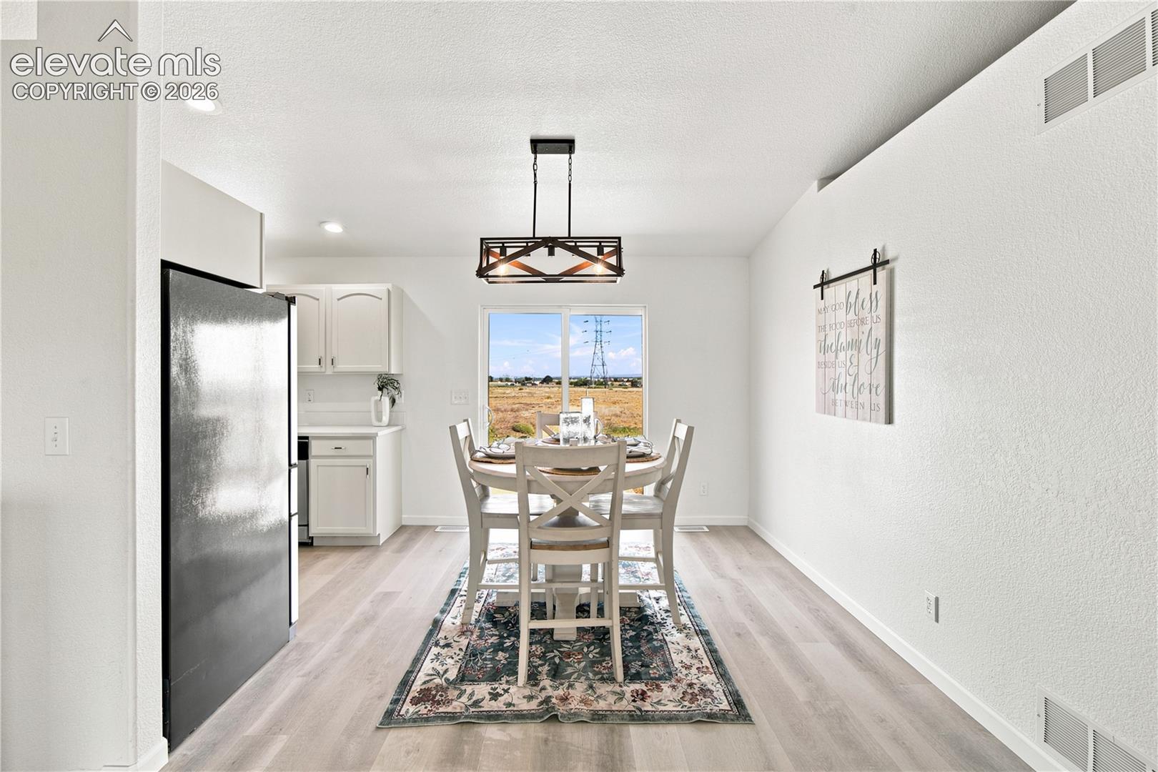 Dining area featuring wood-finish flooring, a contemporary chandelier, and a window framing the outdoor scenery