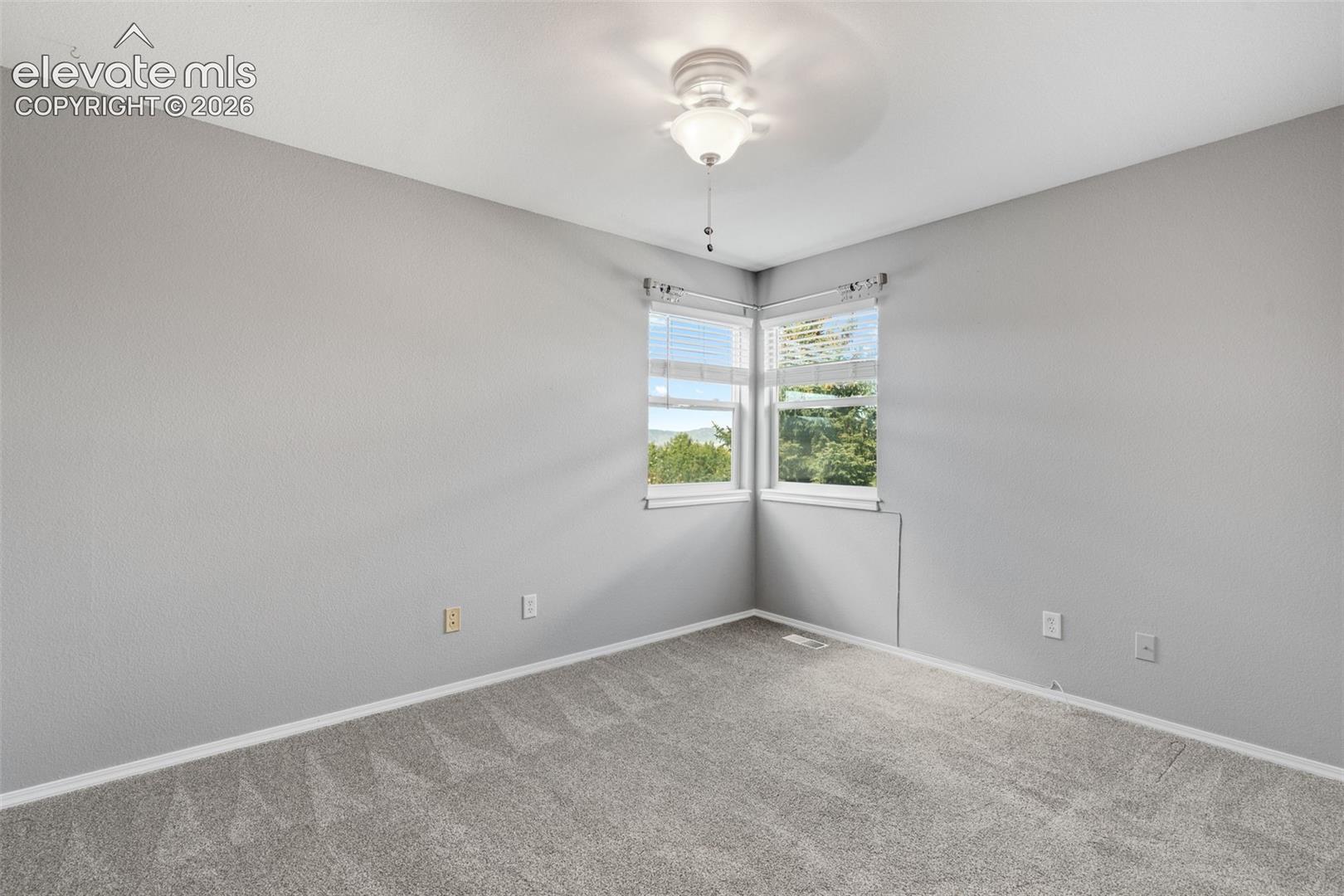 Neutral wall tones, wall-to-wall carpeting, ceiling-mounted light fixture with fan, and corner windows