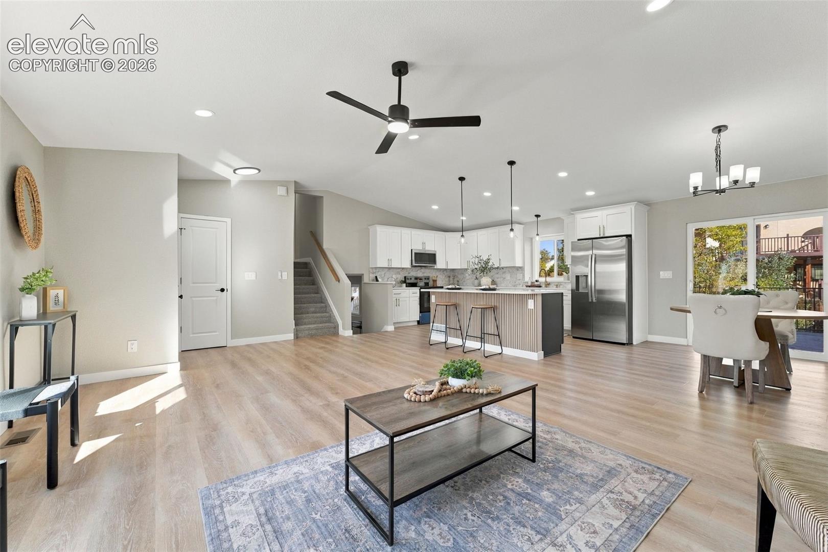 Open-concept interior featuring wood-finish flooring, a kitchen island with pendant lighting, white cabinetry, stainless steel appliances, and a glass sliding door