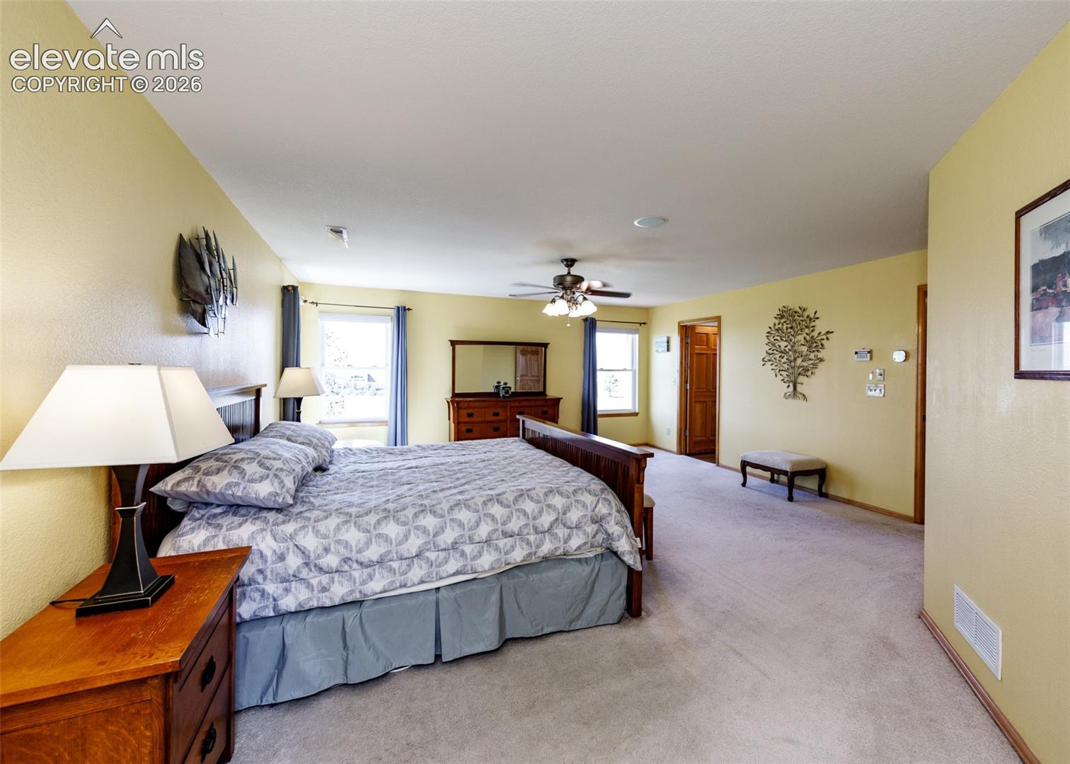 Spacious room featuring carpeted flooring, multiple windows with drapes, a ceiling fan, and solid wood interior doors