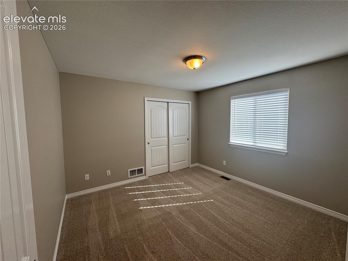 Neutral-toned room featuring wall-to-wall carpeting, dual-panel closet doors, and a window with horizontal blinds